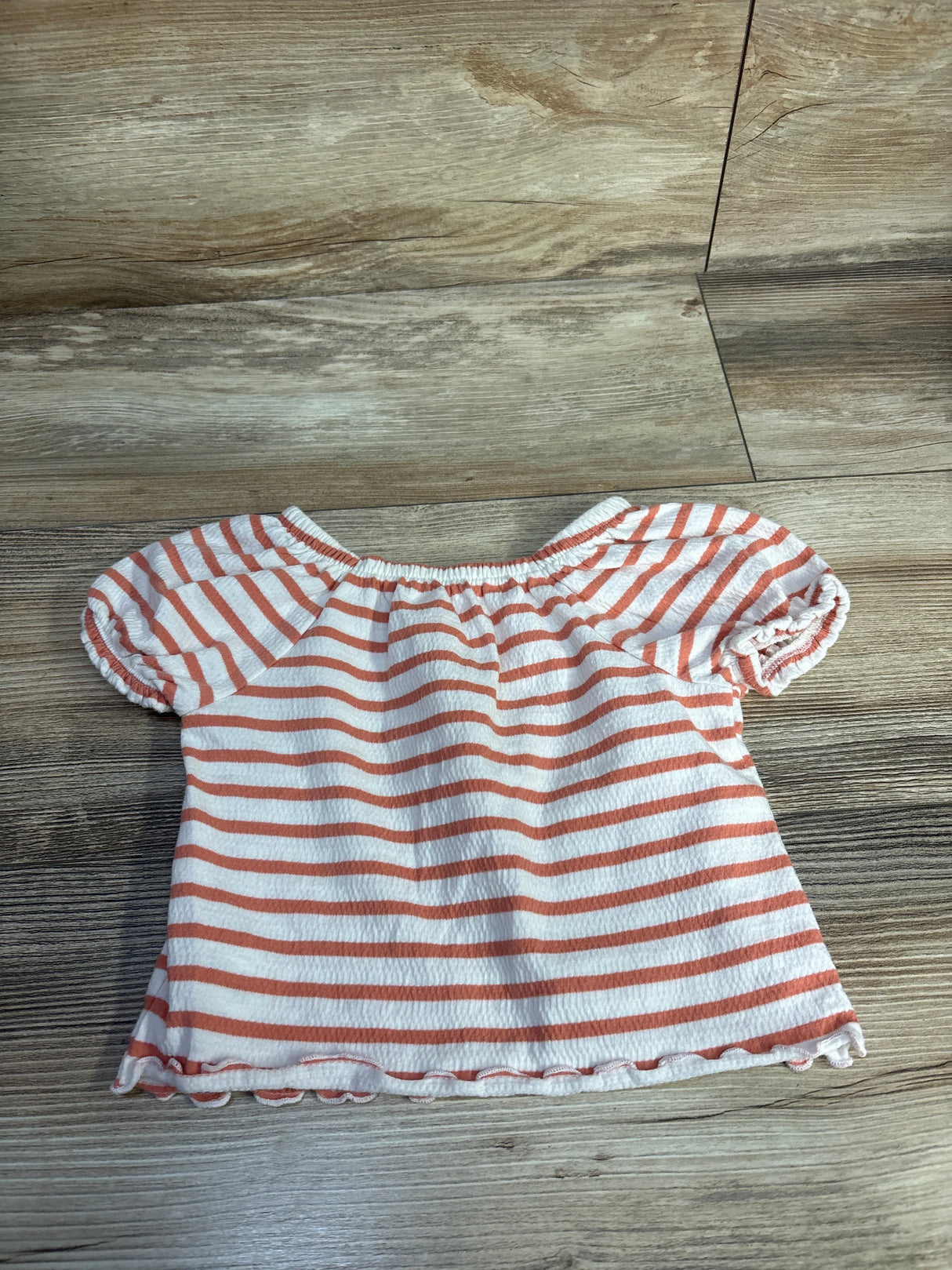 Flat lay of toddler white shirt with orange horizontal stripes and puff sleeves, elastic gathered neckline on wood floor