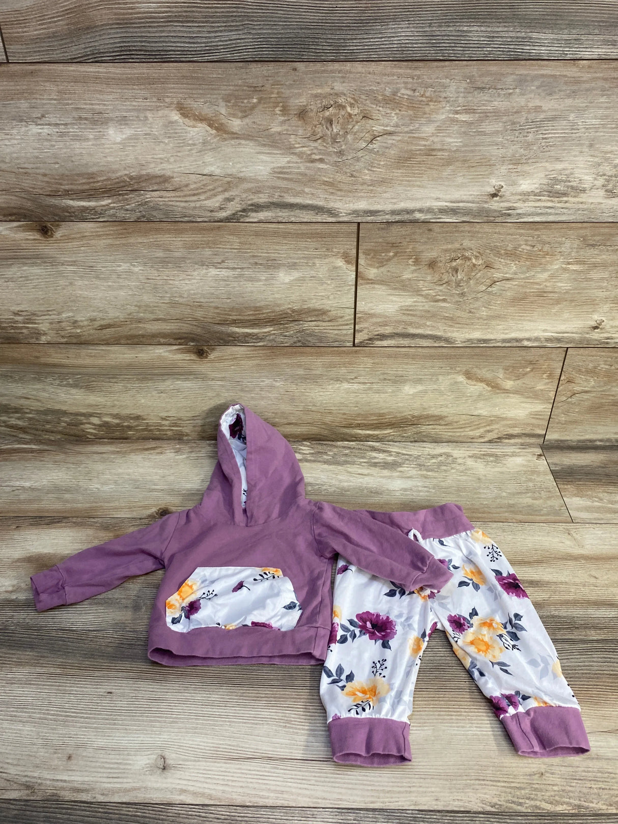 Flat lay of purple baby hoodie and floral pants set (3-6 months) showing floral-lined kangaroo pocket and cuffed pant legs on wood background