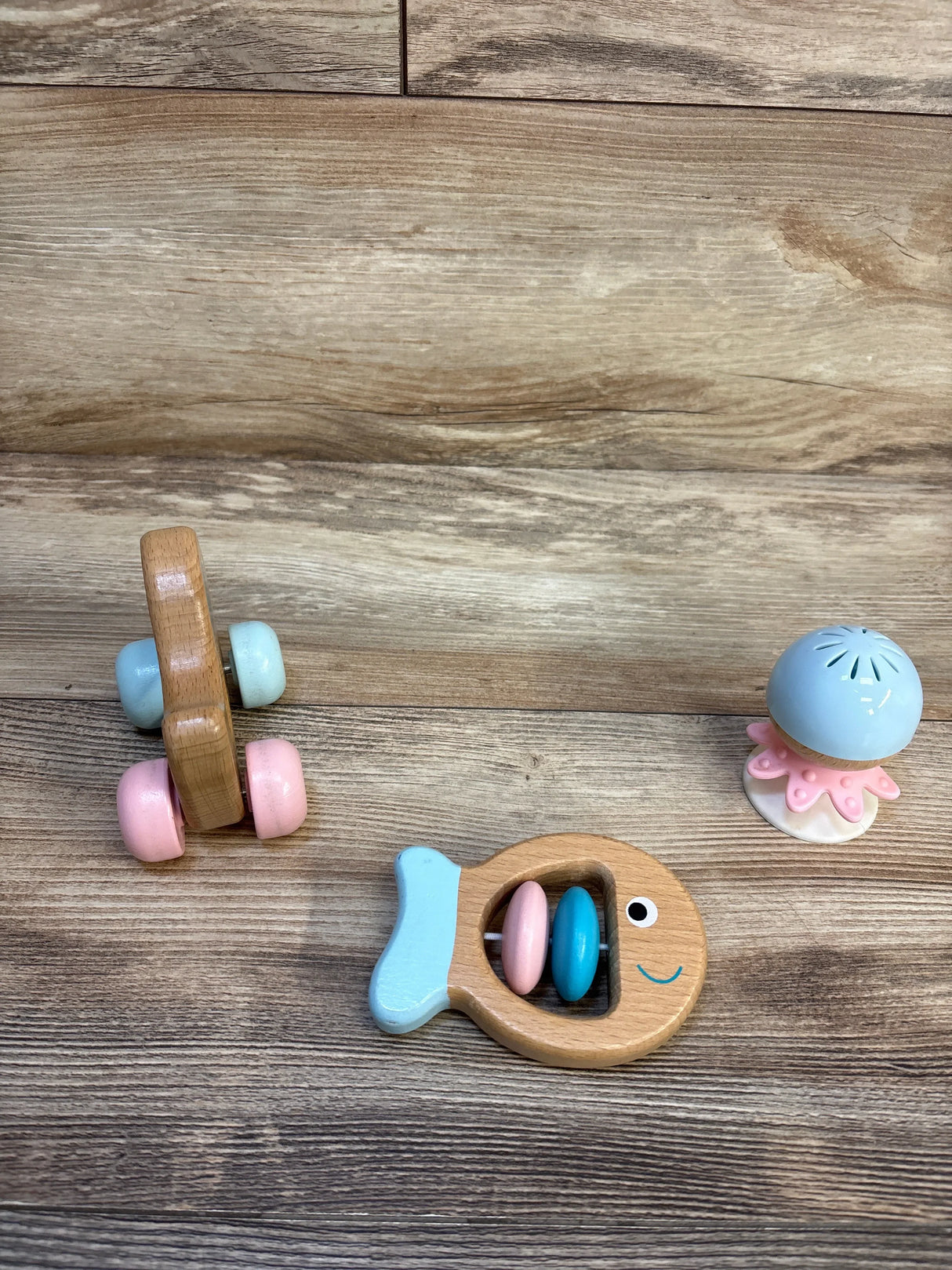 Overhead view of Hape Multi Sensory Wooden Toys 3pk showcasing fish rattle, stay put rattle, and dog on wheels on a wood floor