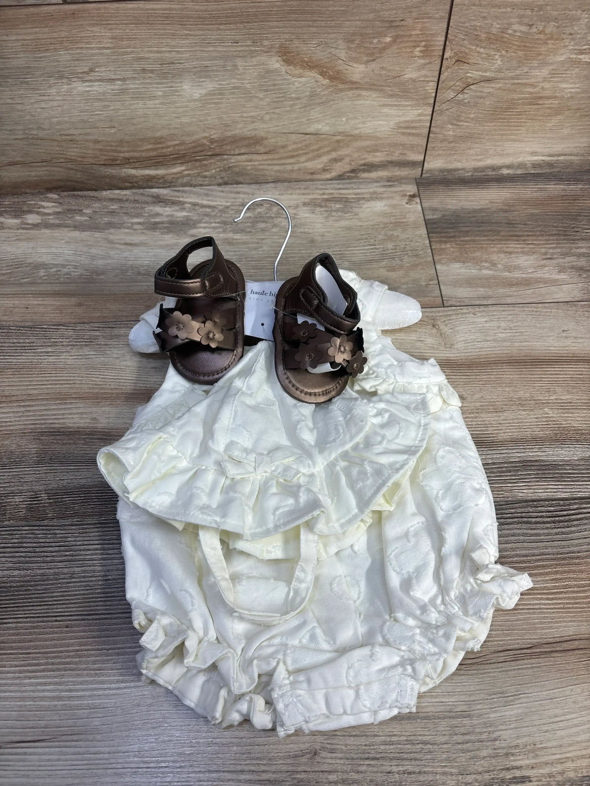 Top view of white Haute Hippie 3-piece layette set showing ruffled romper, bucket hat, and brown sandals on wood floor