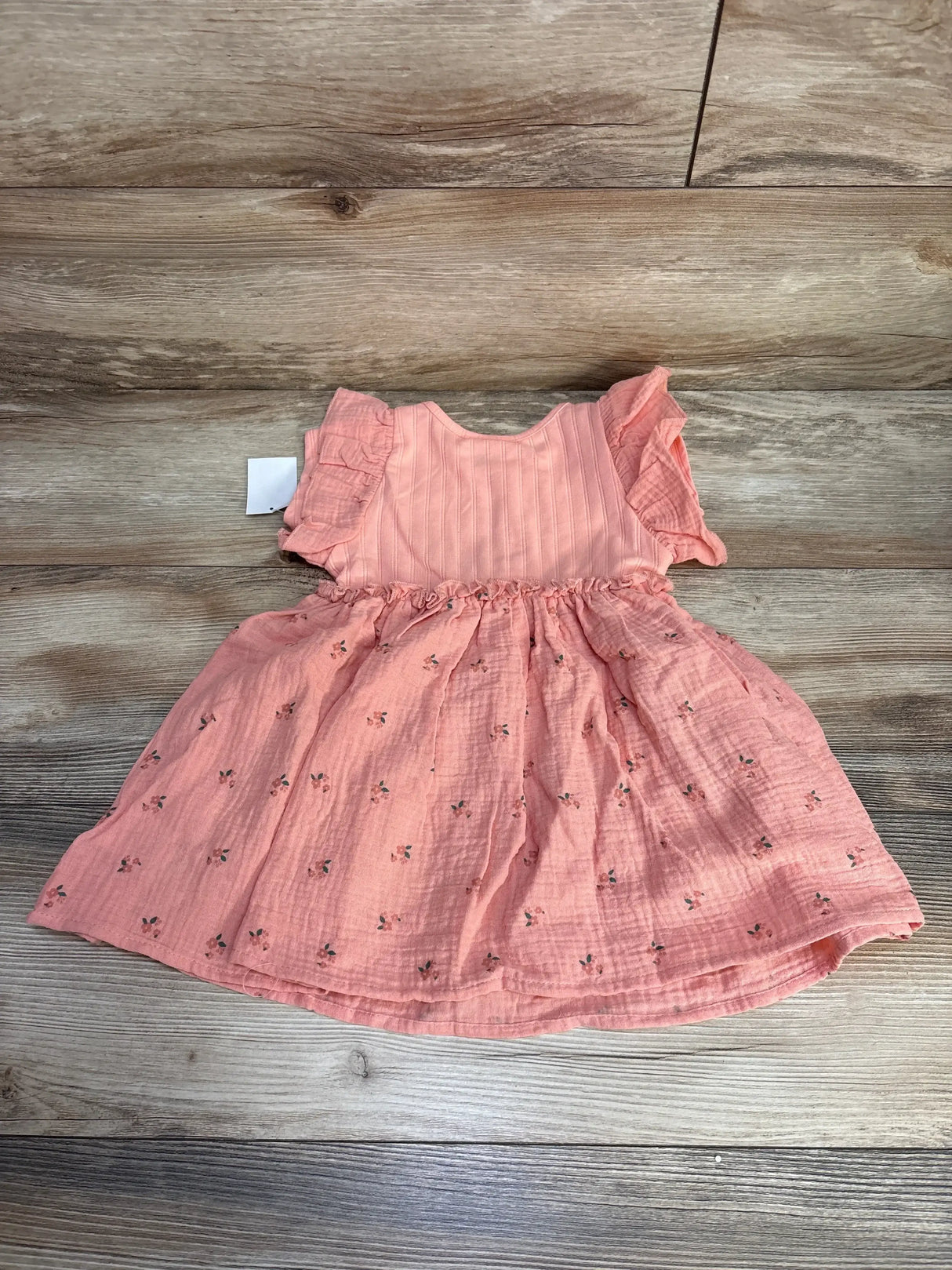 Flat lay of NEW Disney Junior Minnie Mouse Floral Muslin Dress Pink sz 2T showcasing flutter sleeves and floral print muslin with hangtag on wood plank background