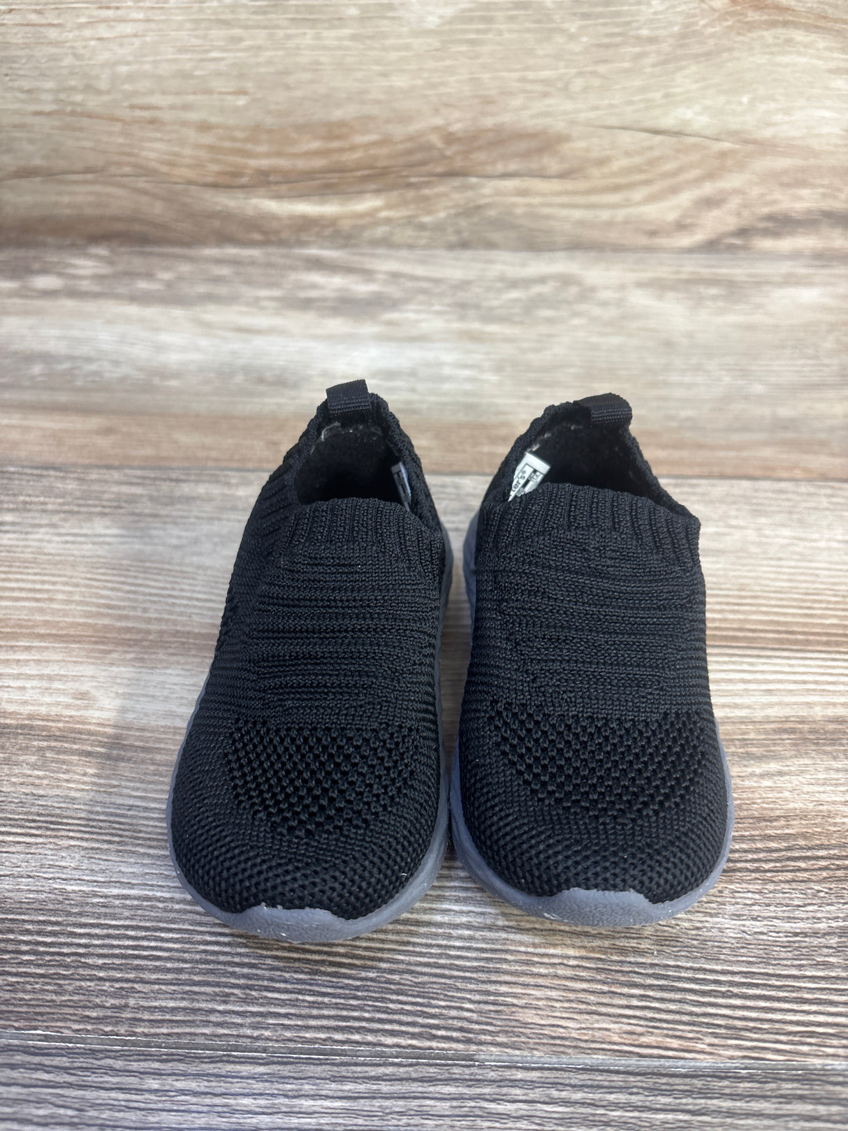 Front view of Carter’s Taylen pull-on athletic sneakers showcasing black knit uppers and gray soles on a wood-grain background