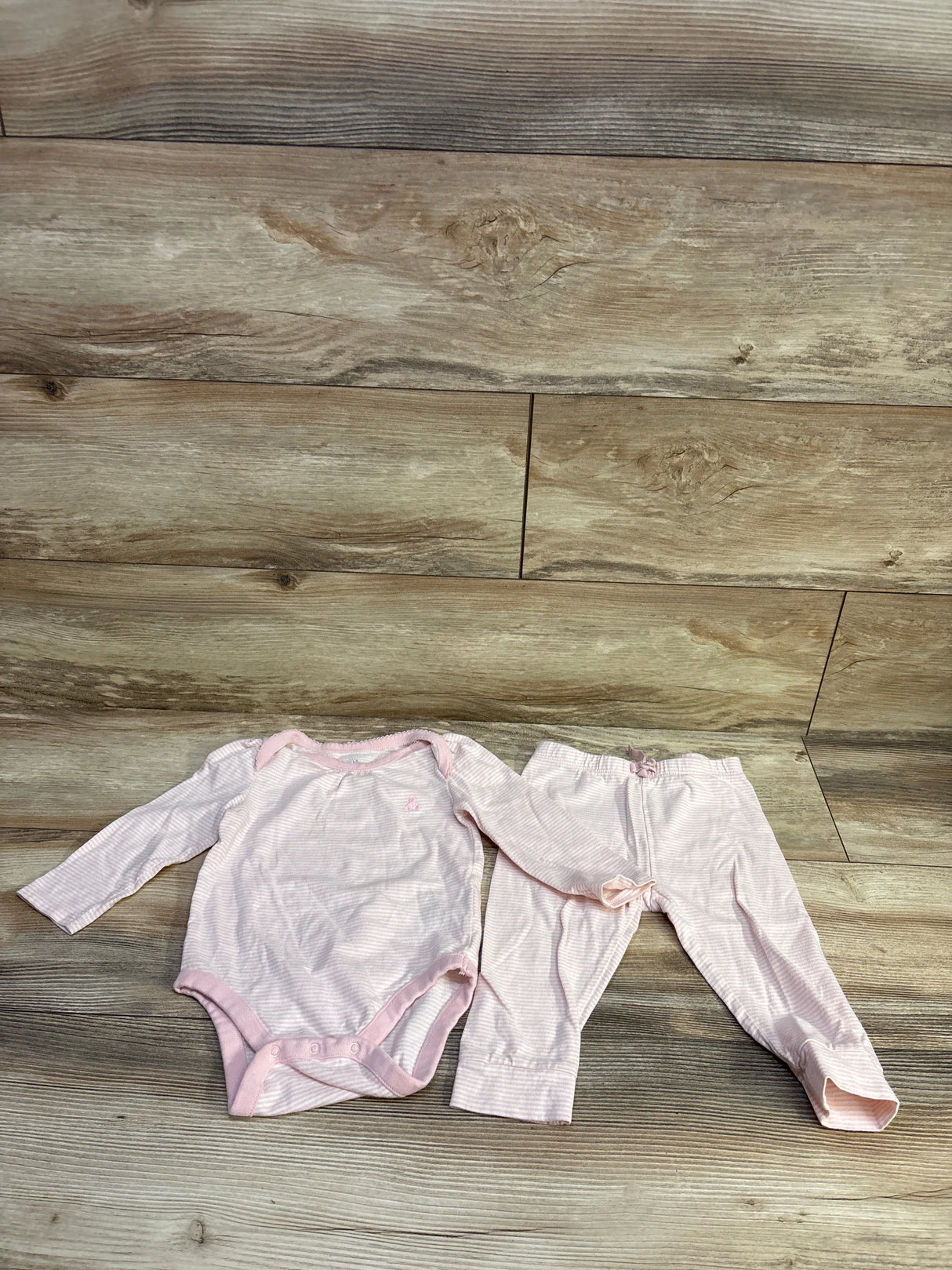 Flat lay of pink-and-white striped 2-piece bodysuit and pants showing long sleeves, snap crotch, and elastic waist on wood background