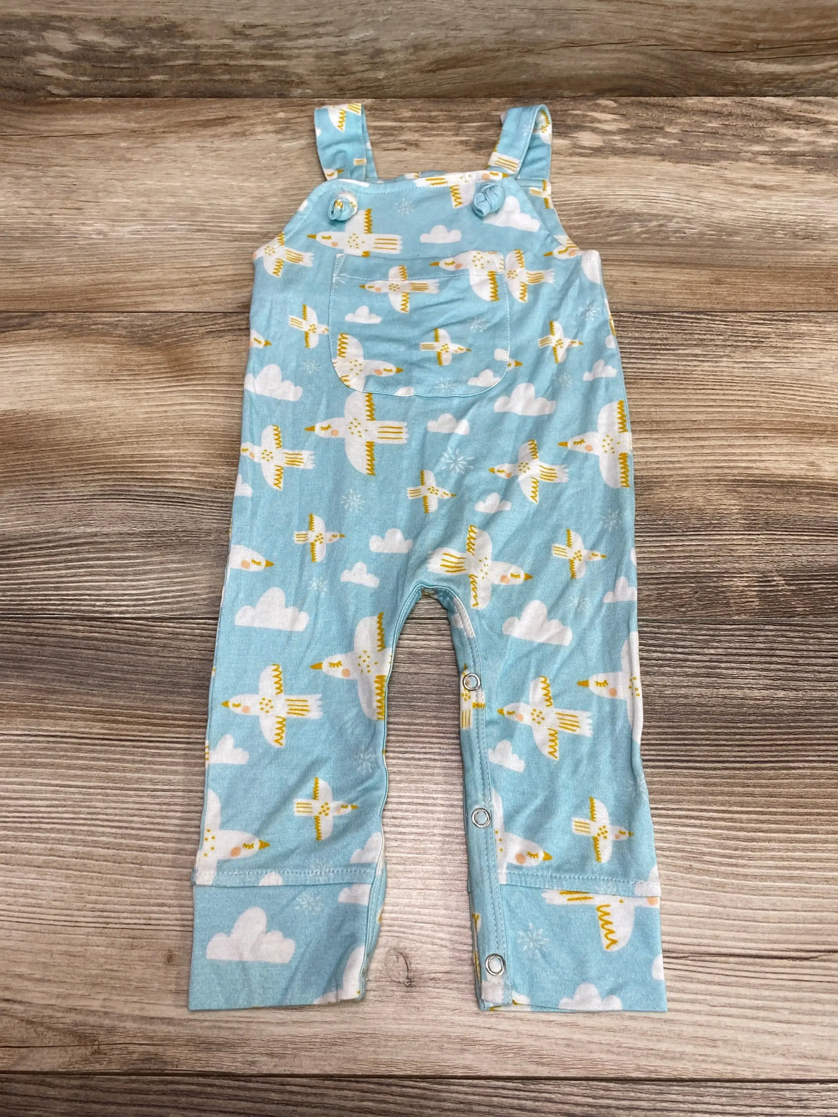 Flat lay of blue baby overalls with yellow-and-white bird print, front chest pocket and snap leg closures on wood background