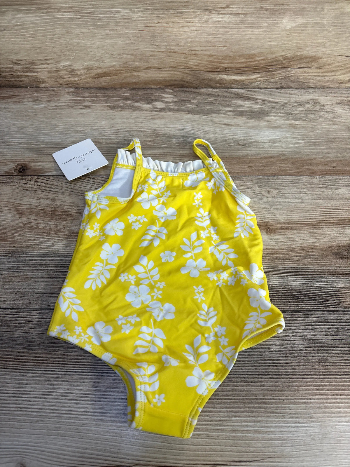 Front view of Starting Out one piece swimsuit in yellow showcasing white floral pattern with wood background