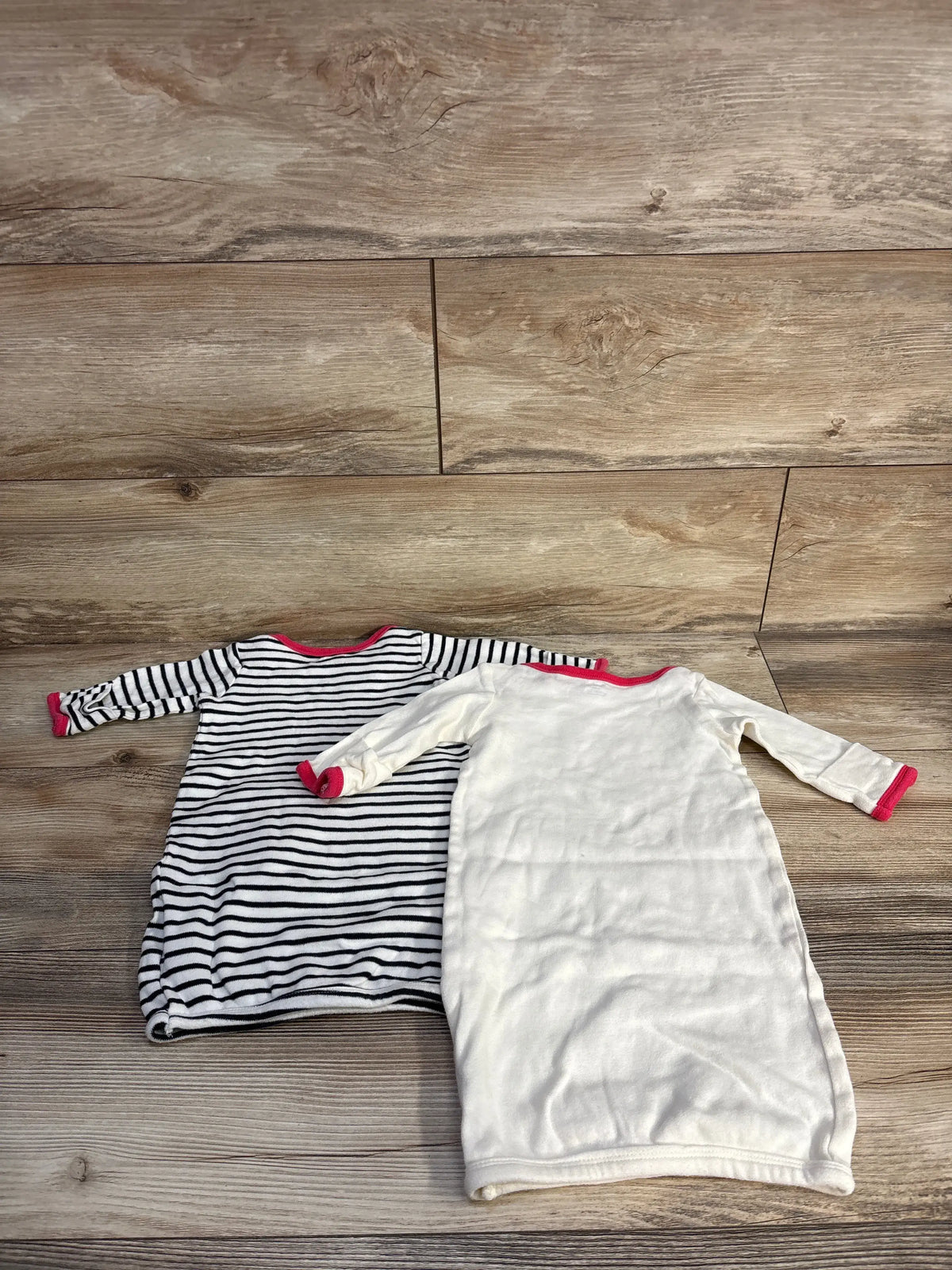 Overhead view of Touched By Nature two-pack sleep gowns, showing striped and cream gowns with red trim on a wood floor