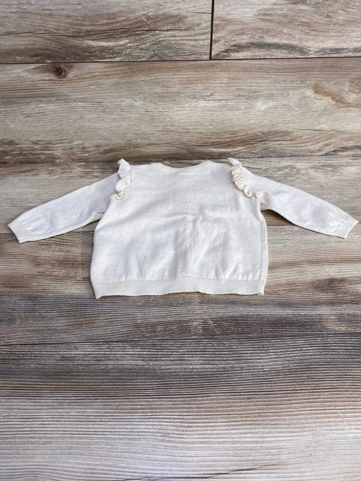 White long-sleeve toddler sweater with ruffle details on wooden floor background
