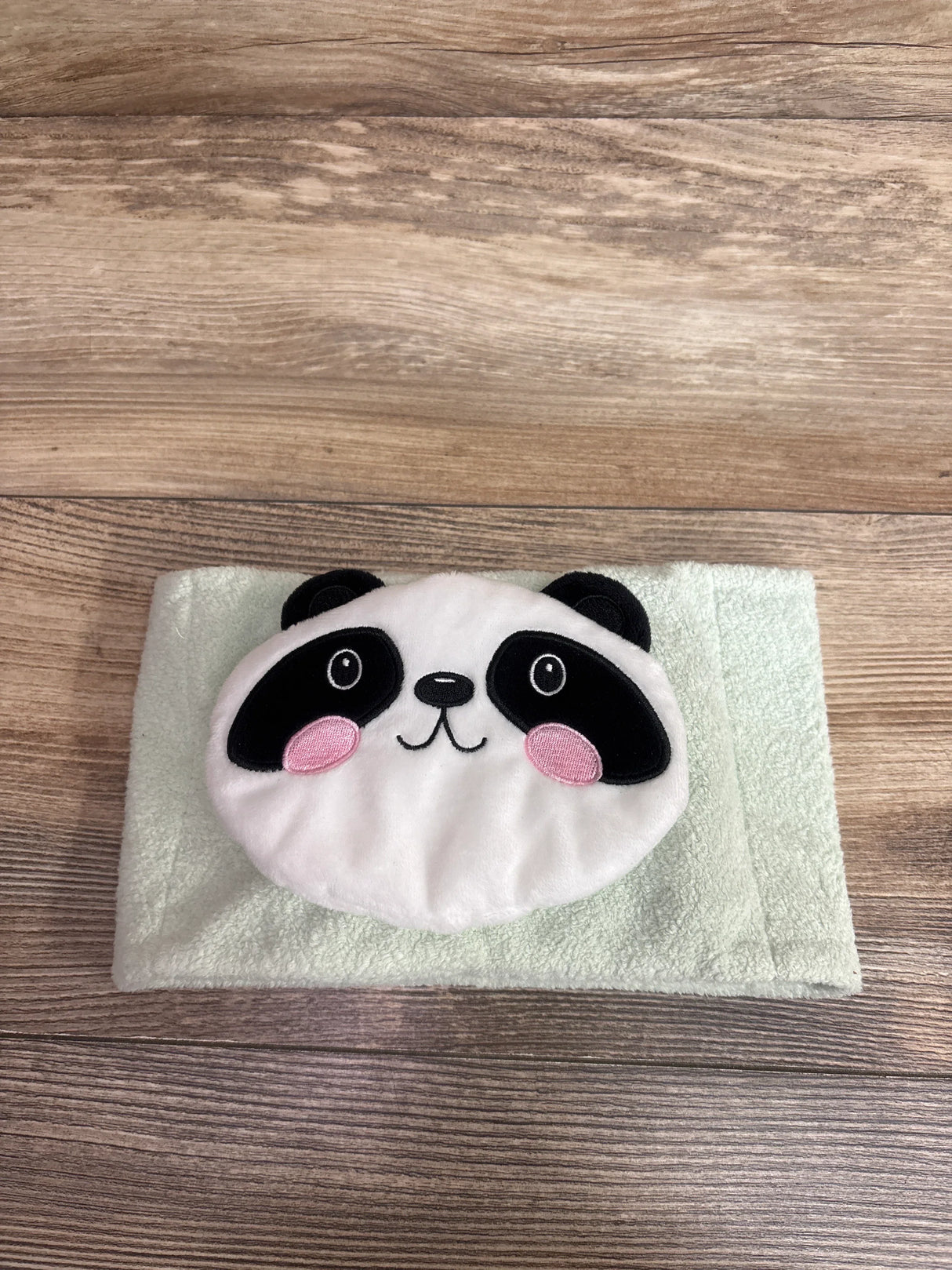 Top view of Dr. Brown’s Infant Gripebelt heated belly band showcasing panda face applique on folded light green towel on wooden surface