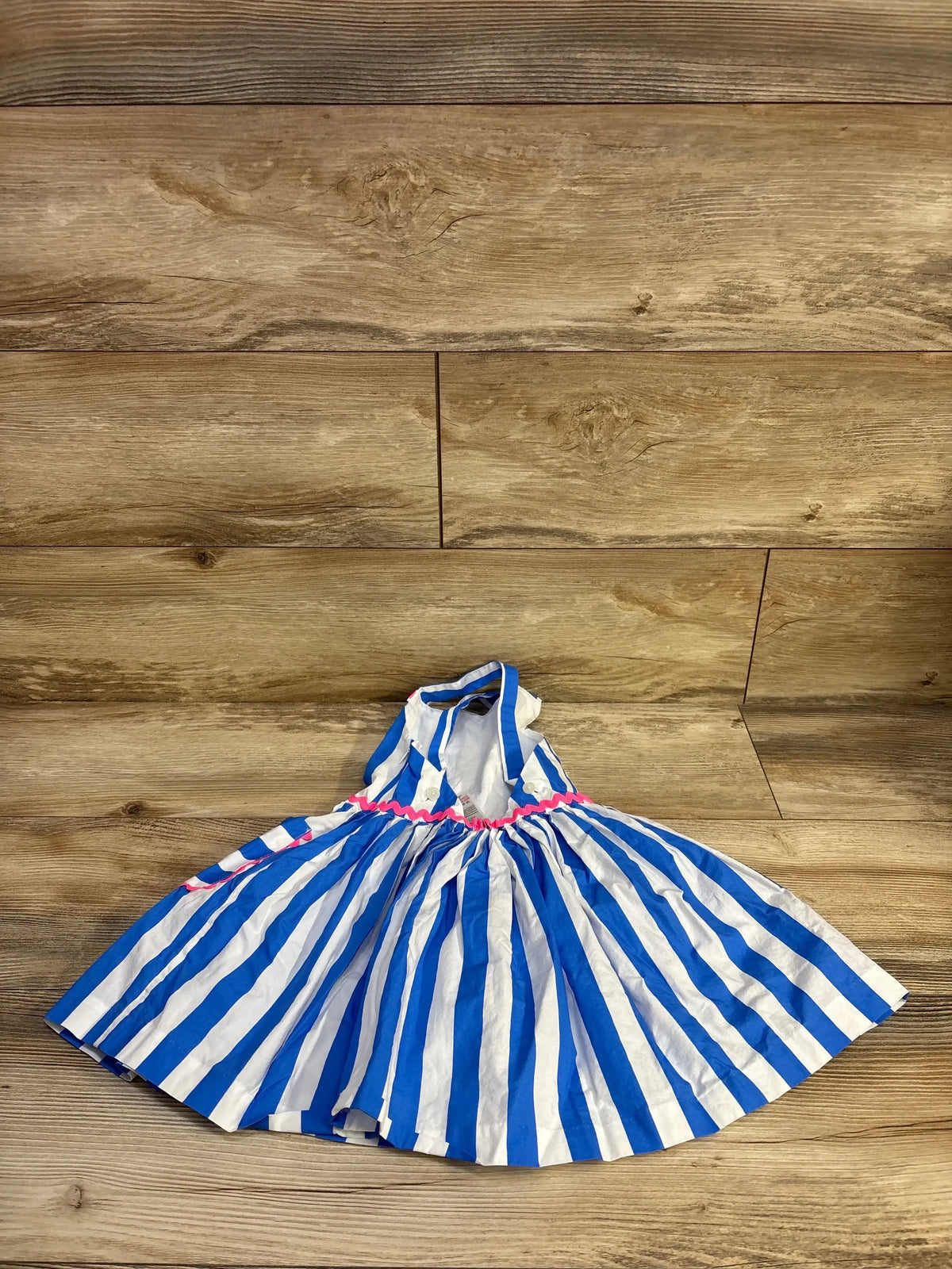 Top-down view of blue and white striped Jacadi toddler halter dress showing pink ric-rac waist trim and full gathered skirt on wood floor