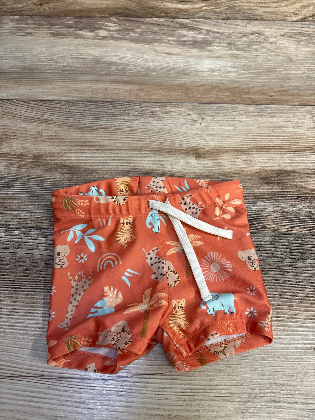 Front view of H&M orange animal print swim shorts showcasing the elastic waistband and white drawstring on a wood surface