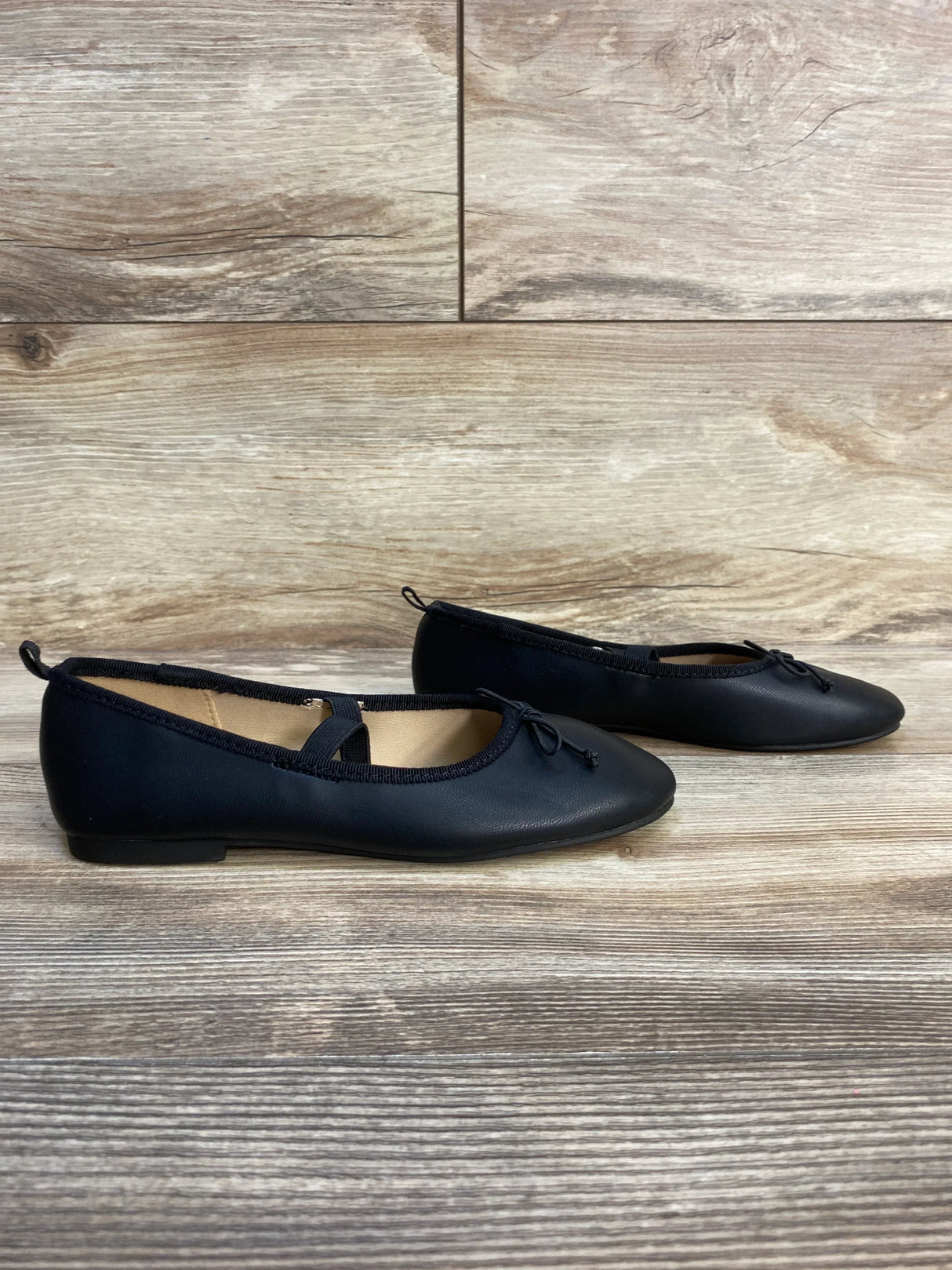 Black girls ballet flats with bow and elastic strap on wood floor