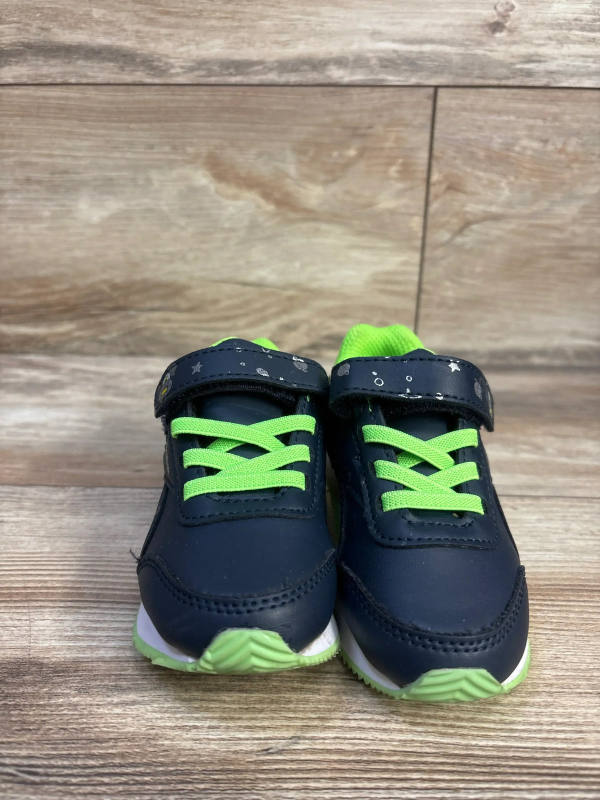 Front view of Reebok Space Sneakers in navy and green showcasing green laces and hook and loop closures on a wood floor