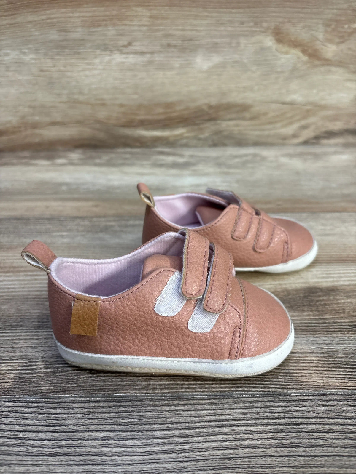 Close-up view of Rokment pink non-slip crib shoes showcasing double hook-and-loop straps and pull tabs on a wood-grain surface