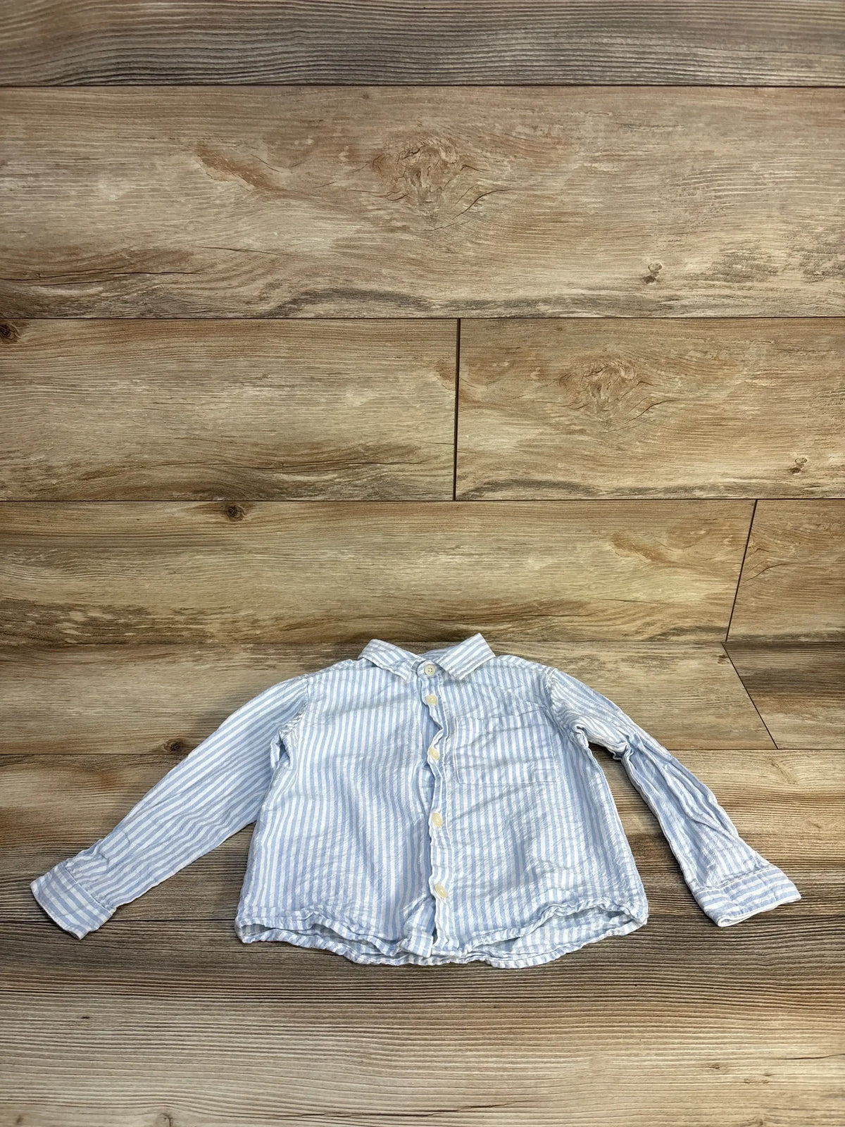 Light blue and white striped long sleeve button-up shirt for toddlers on wood background