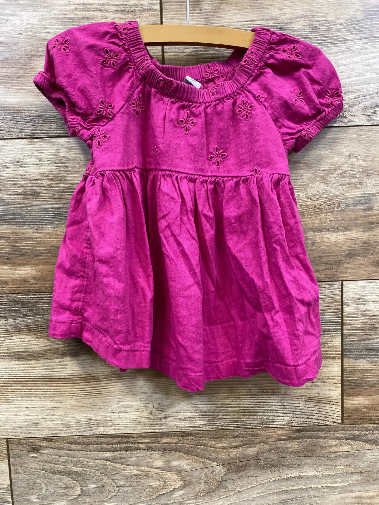 Front view of Old Navy toddler eyelet dress in boysenberry pink with puff sleeves, gathered skirt, and elastic neckline on wood background