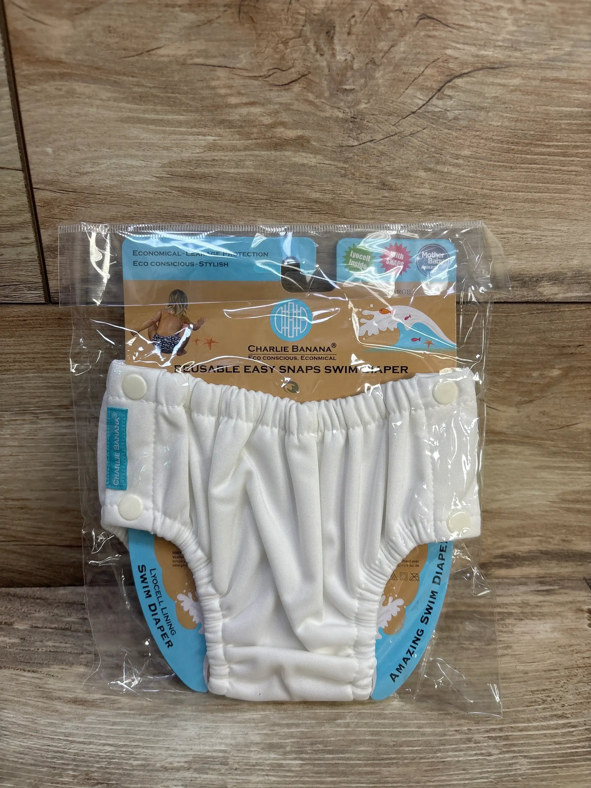 Front of white Charlie Banana swim diaper size L (18–36 mo) with side snaps and elastic leg openings on wood