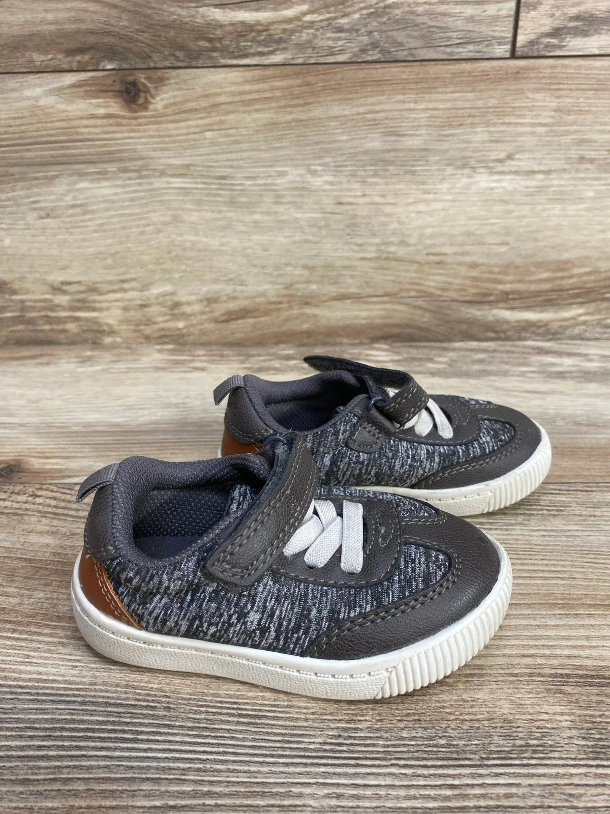 Gray toddler sneakers with white soles, white laces, and brown heel detail on wooden floor