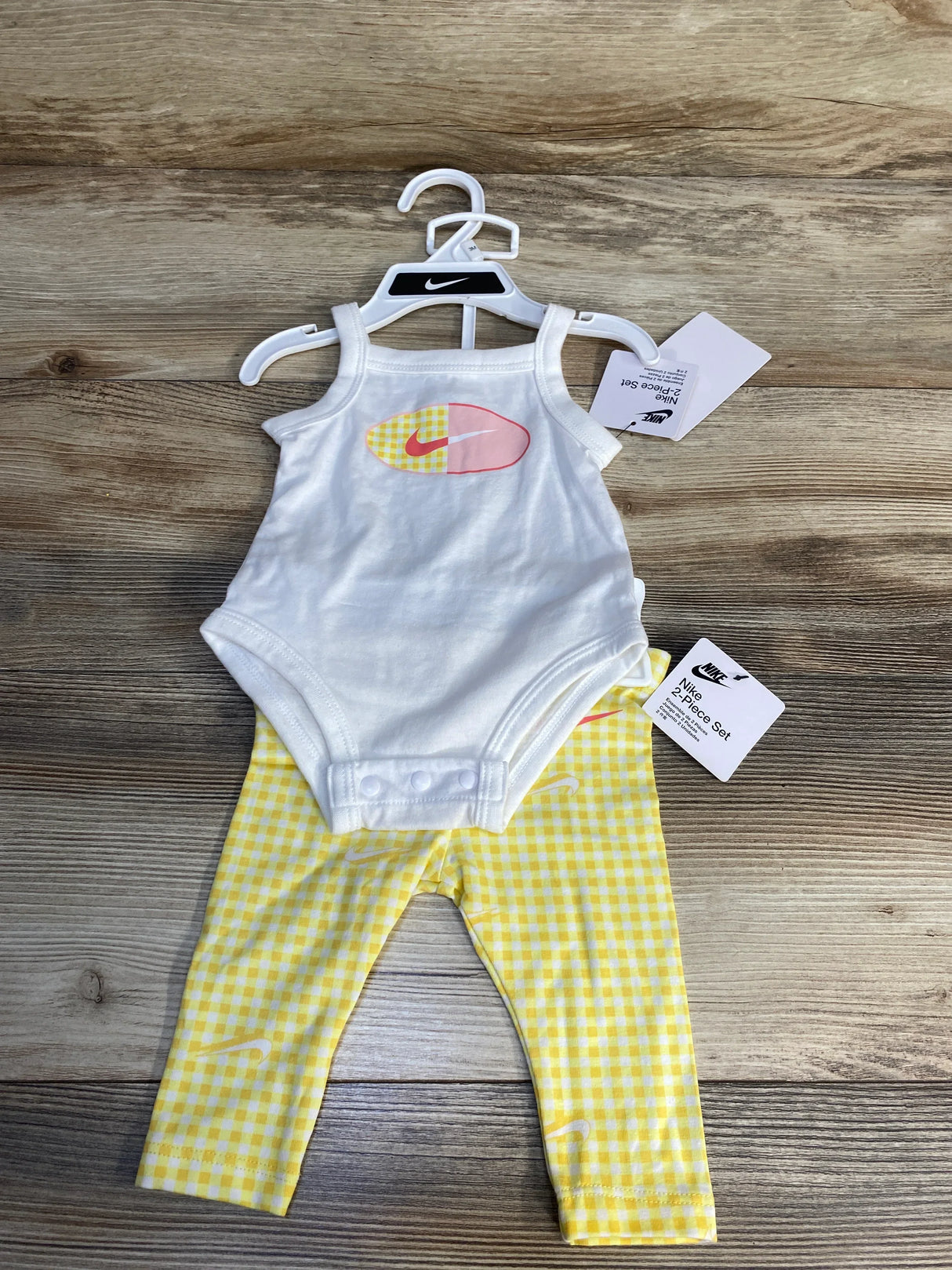 Nike baby outfit with white bodysuit and yellow checkered leggings on wooden background
