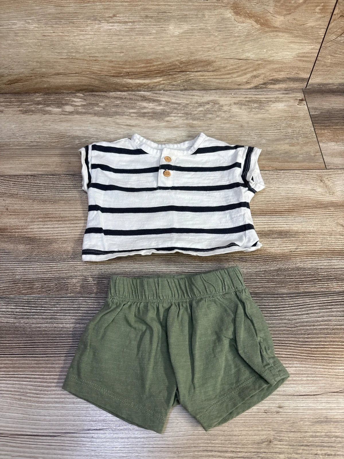 Flat lay of newborn white and navy striped henley shirt with wooden buttons and olive shorts with elastic waist on wood
