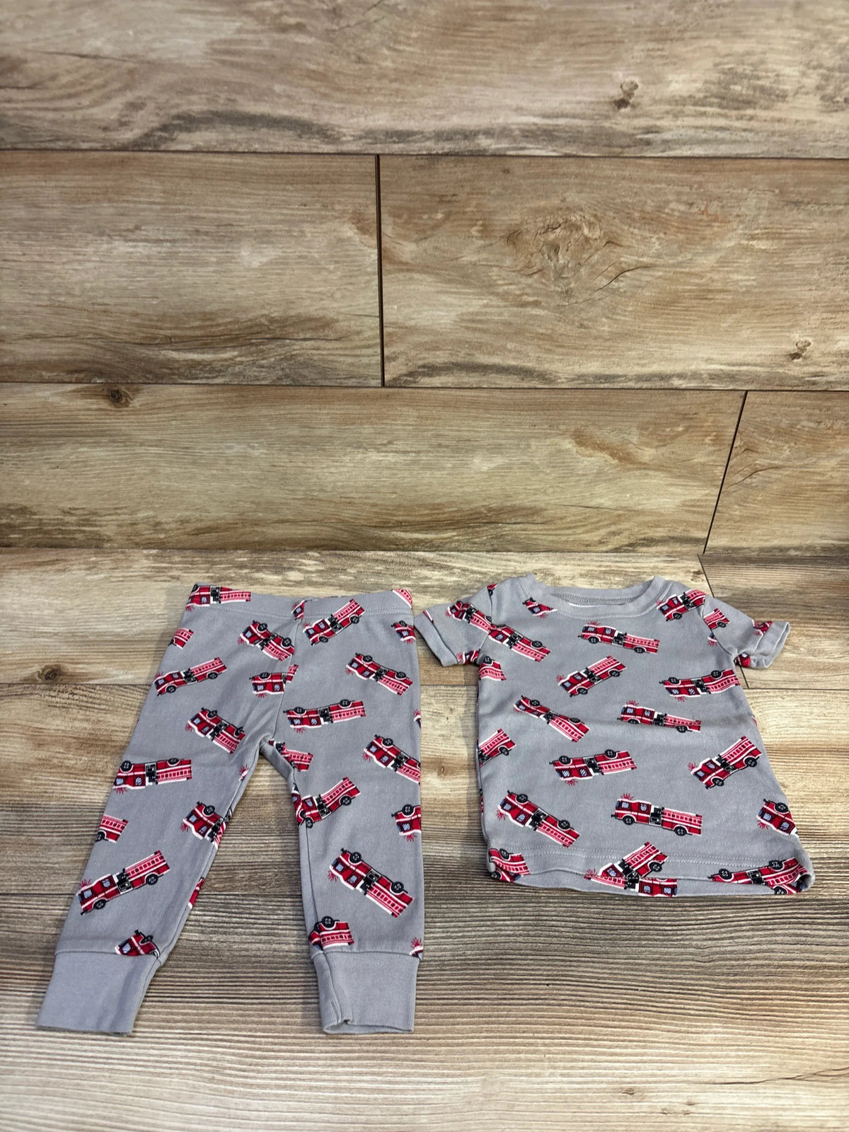 Flat lay of grey 2-piece toddler pajama set with red fire truck print, short-sleeve top and cuffed pants on wood background