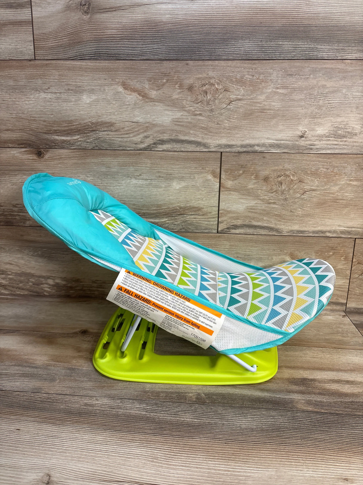 Colorful baby bouncer seat with teal and yellow geometric pattern and green base on wood floor.