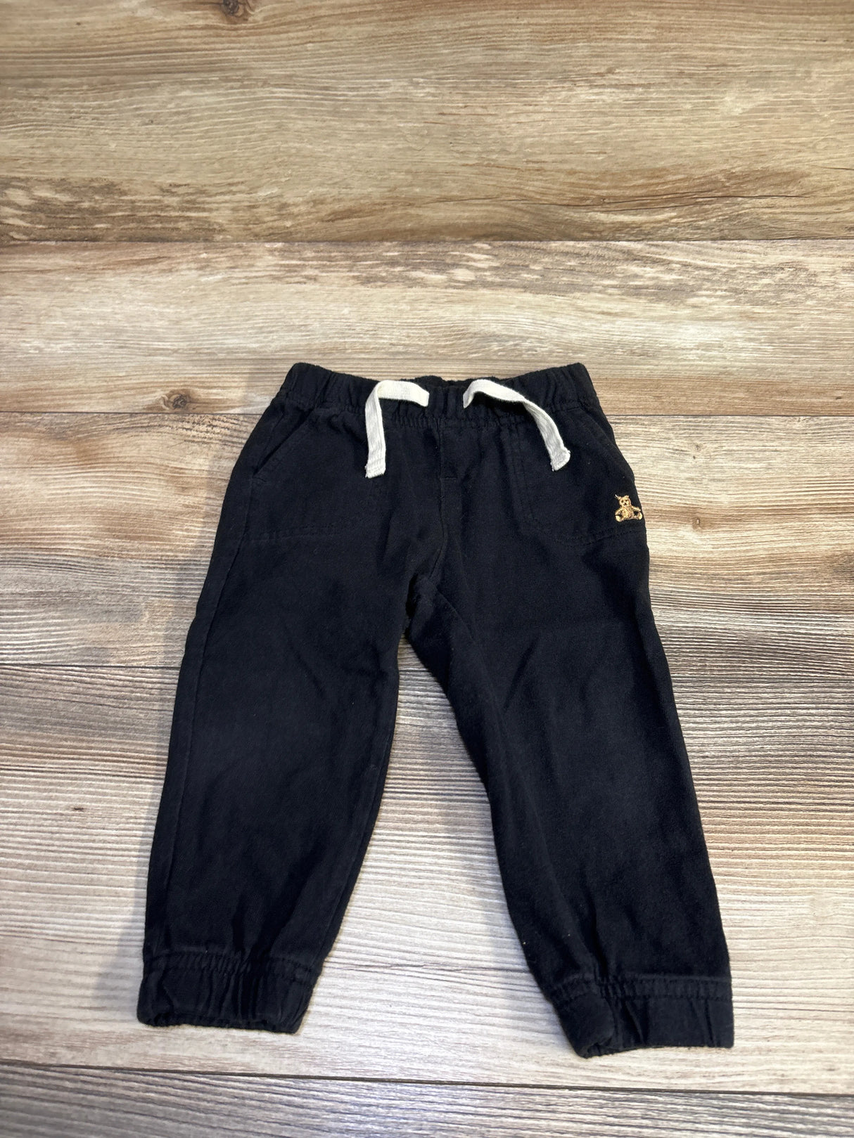 Top view of Baby Gap black joggers size 12 to 18 months showing white drawstring, elastic cuffs, and pockets on wood