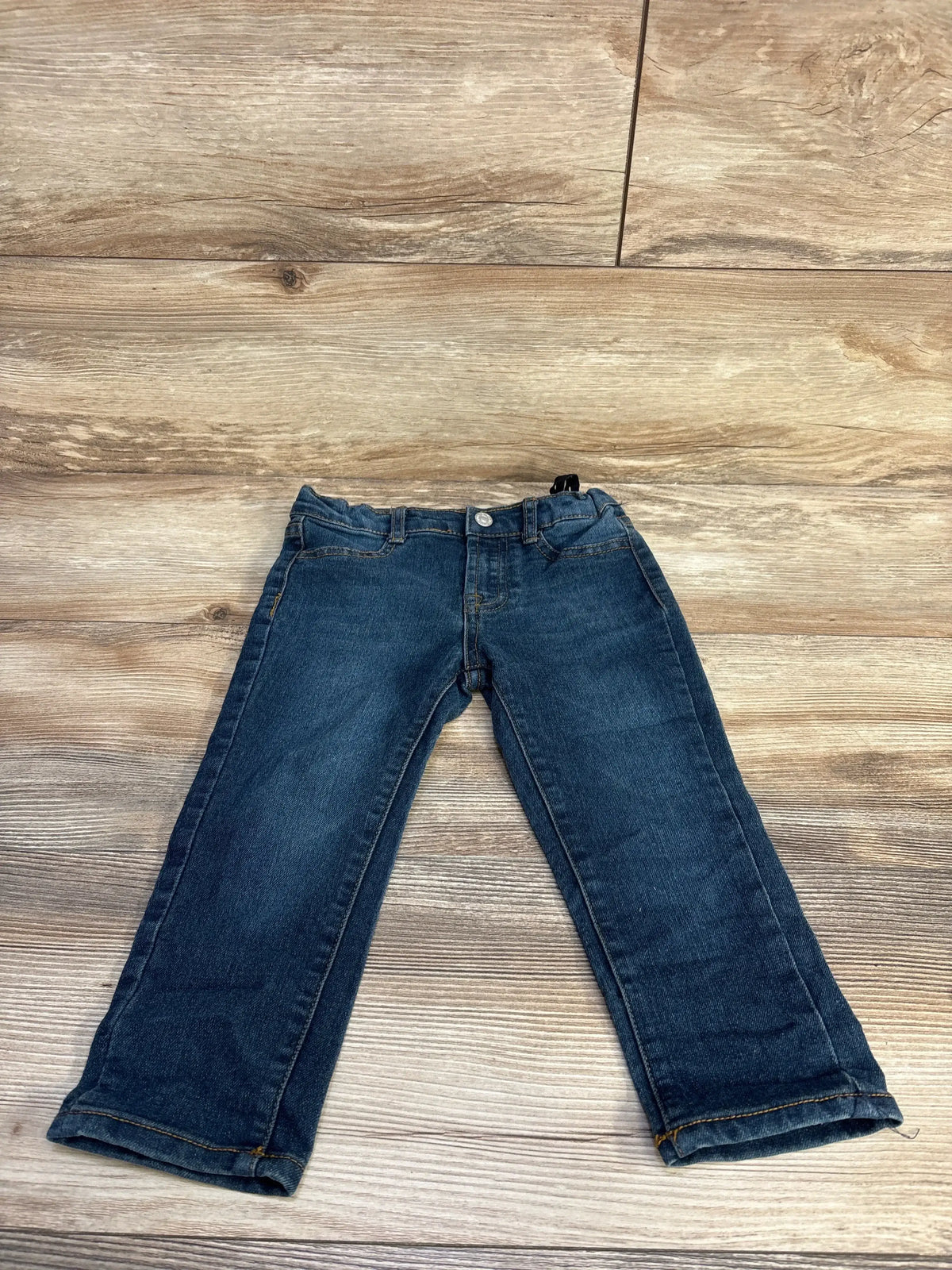 Front view of toddler 7 For All Mankind dark wash jeans showing adjustable elastic waist, front pockets, and rolled cuffs on wood floor