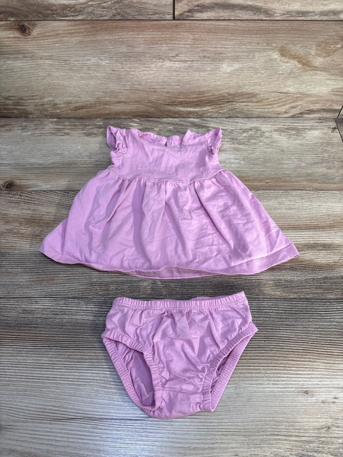 Front view of Carter’s pink two-piece dress and bloomers set with ruffled sleeves and gathered skirt on wood background