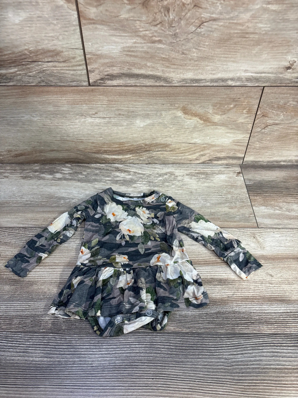 Front view of Gigi & Max bamboo tutu bodysuit in floral camo print with long sleeves and tutu skirt on wood-look floor