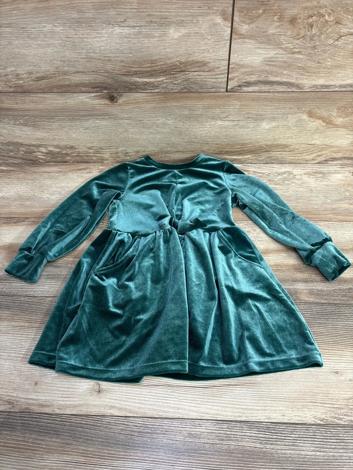 Emerald green velvet long-sleeve toddler dress with pocket detail on wood floor