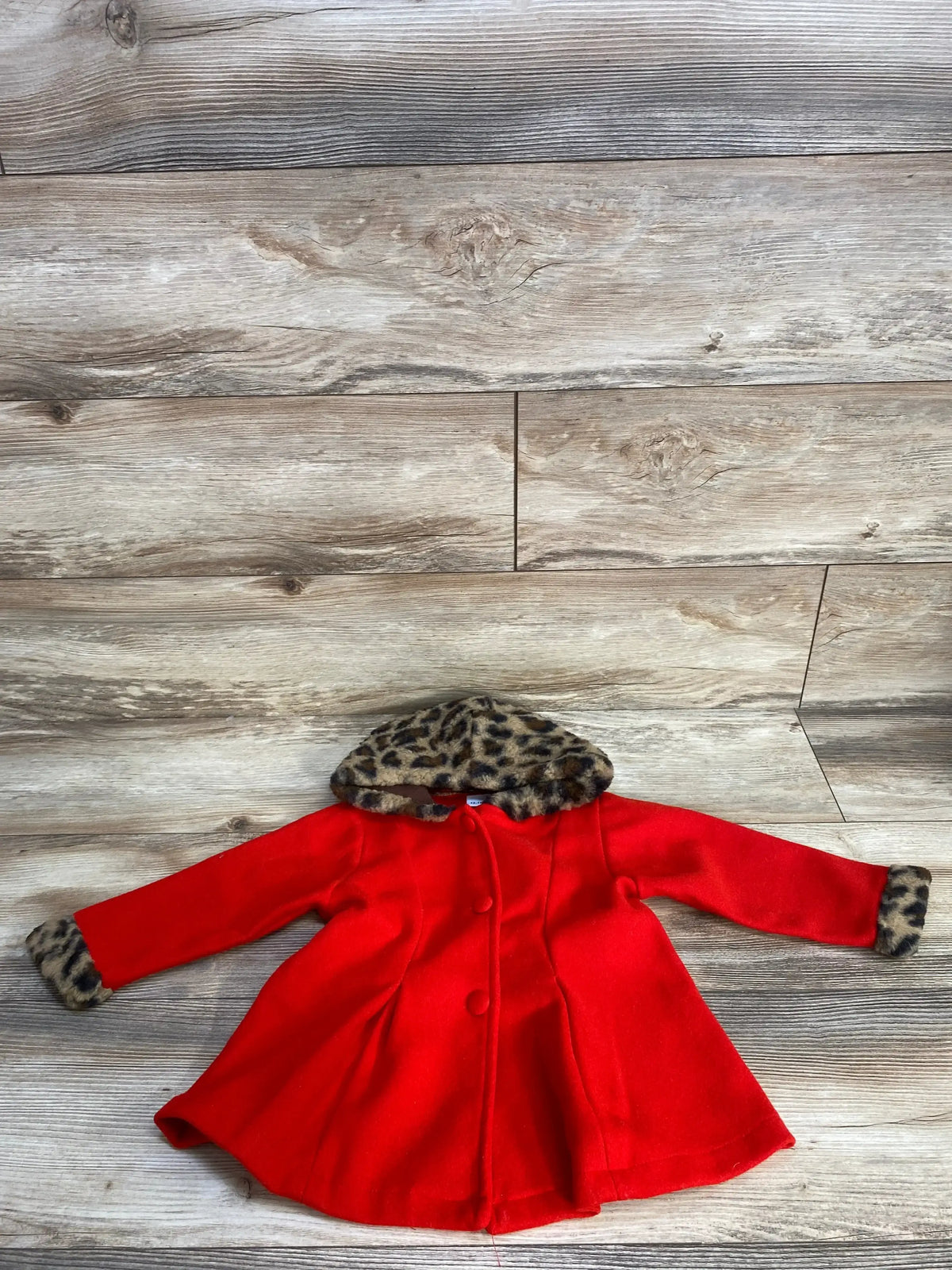 Red coat with leopard print hood and cuffs on wood background