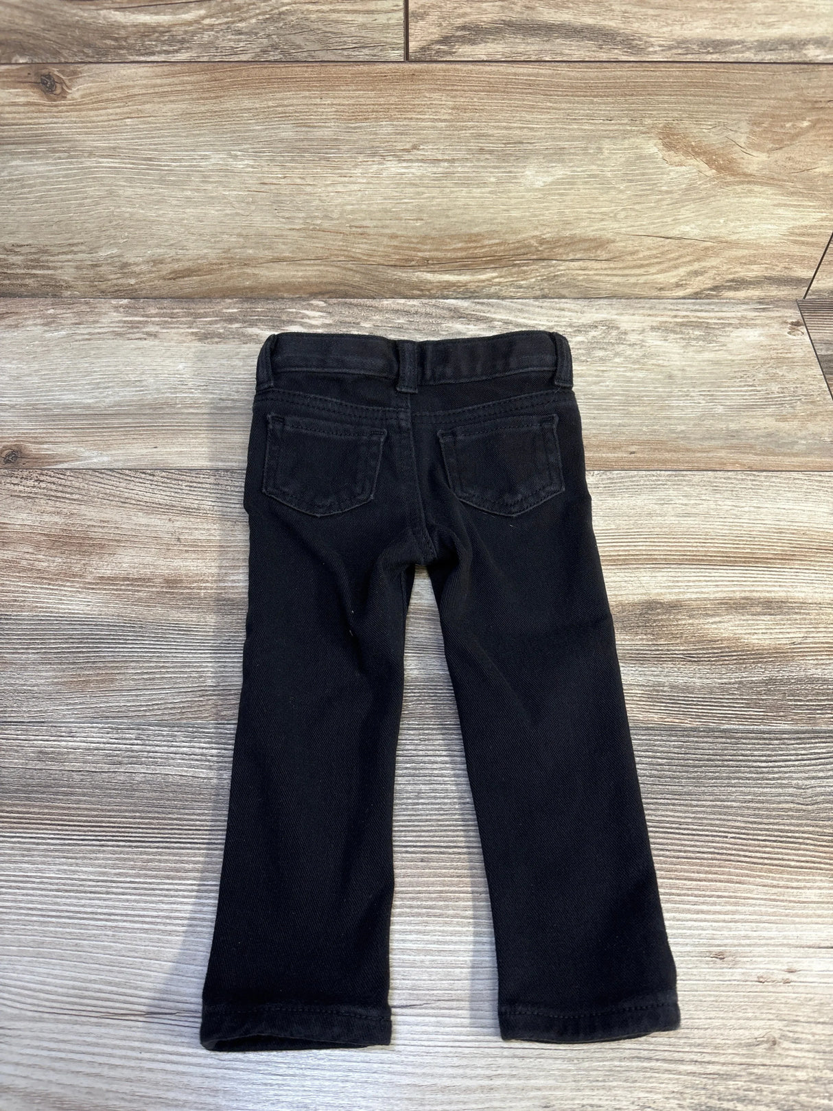 Back view of black Cat & Jack toddler jeggings, size 18 months, showing back pockets and straight legs on a light wood background