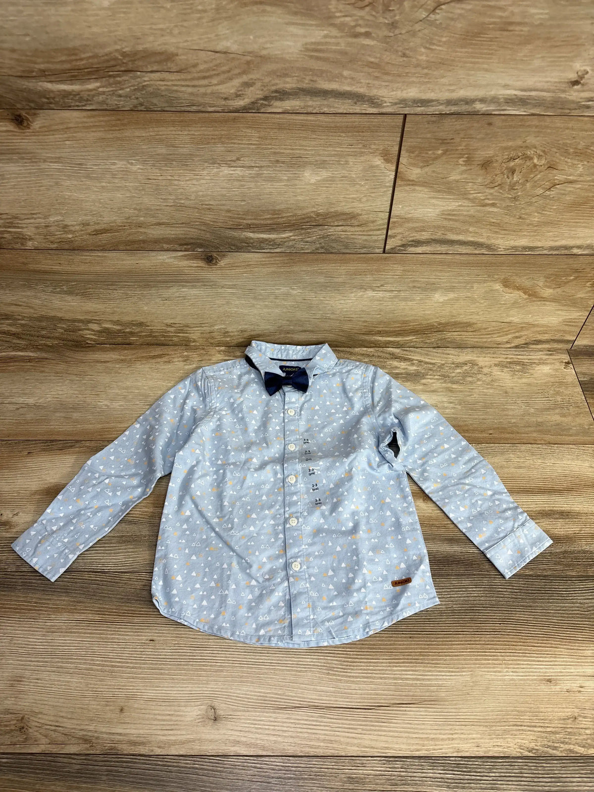 Light blue toddler long-sleeve button-up shirt with white and orange triangle pattern and attached navy blue bow tie on wooden floor