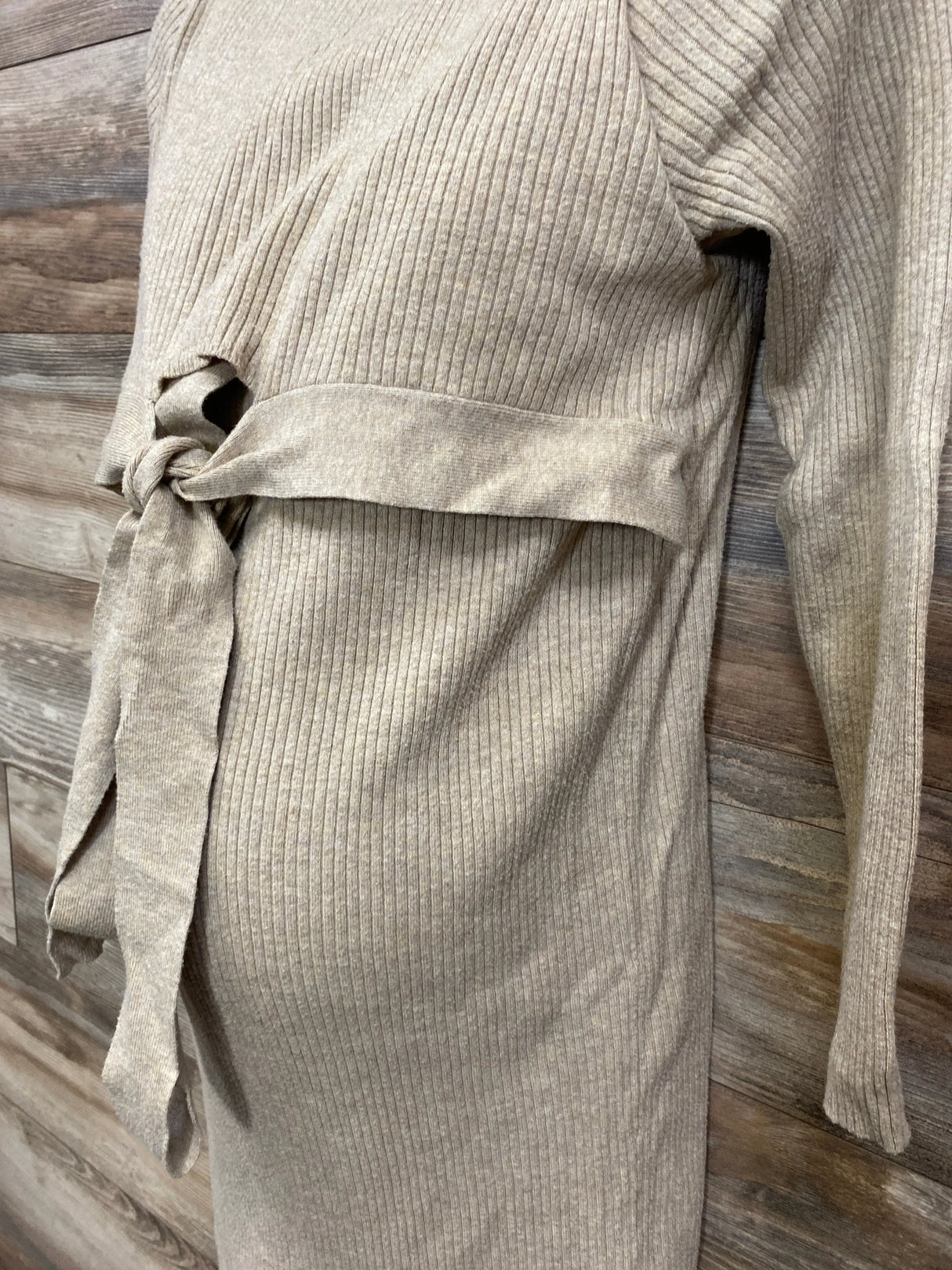 Beige ribbed knit maternity dress with tie waist and long sleeves against wood background