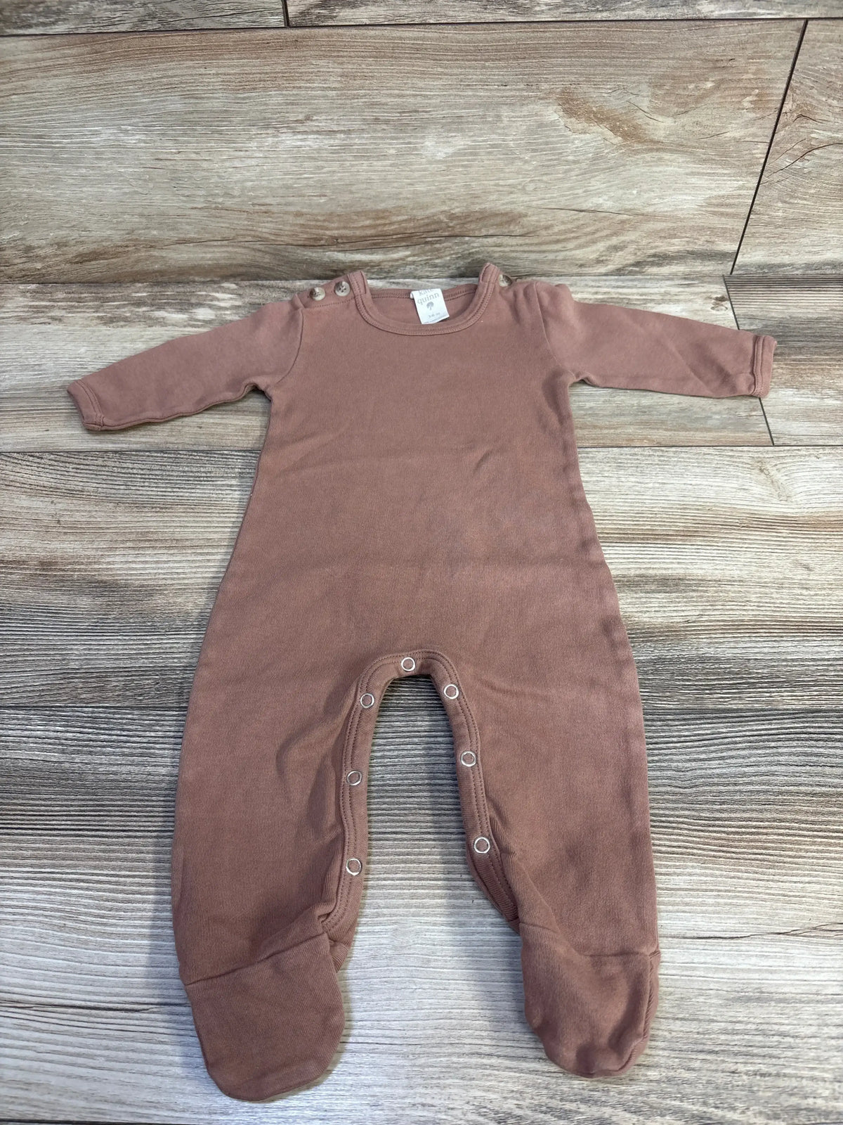 Flat lay of brown Kate Quinn footie coverall showcasing shoulder snaps, snap leg closures and enclosed feet with wood floor