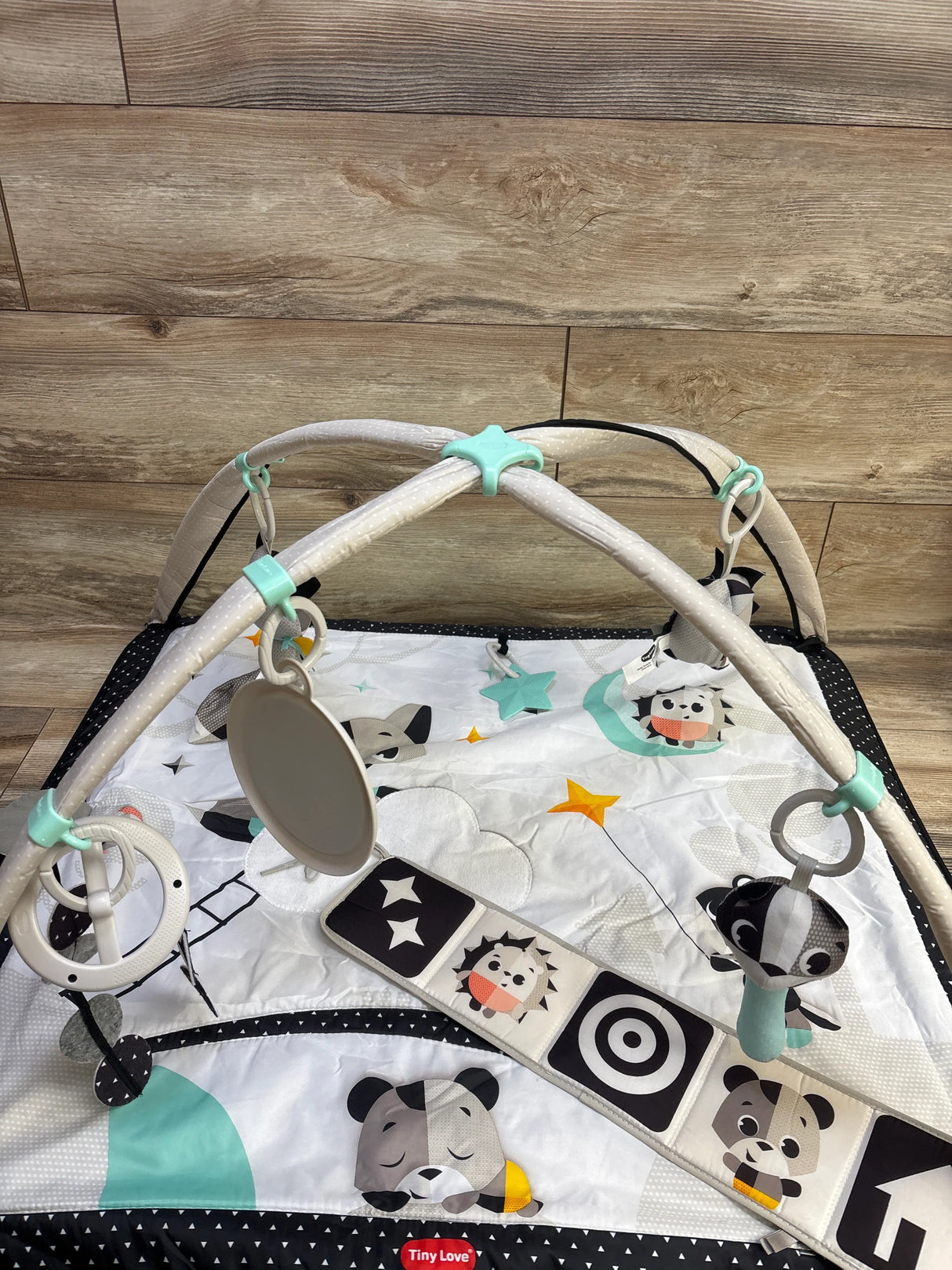 Top down view of Tiny Love Magical Tales Gymini play gym showing crossed arches with hanging toys and mirror on wood floor