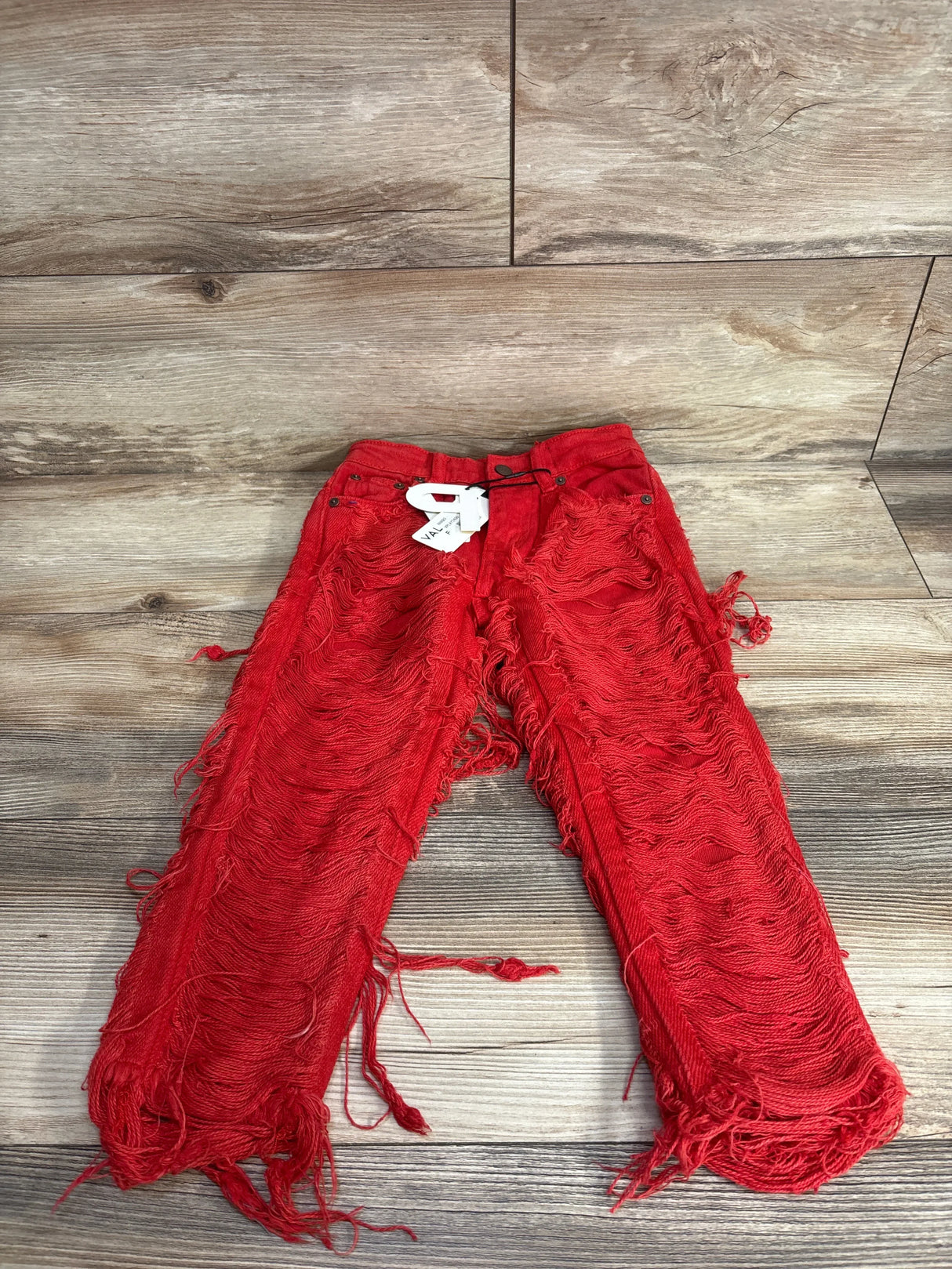 Red distressed kids jeans with fringe detailing, laid flat on wood floor