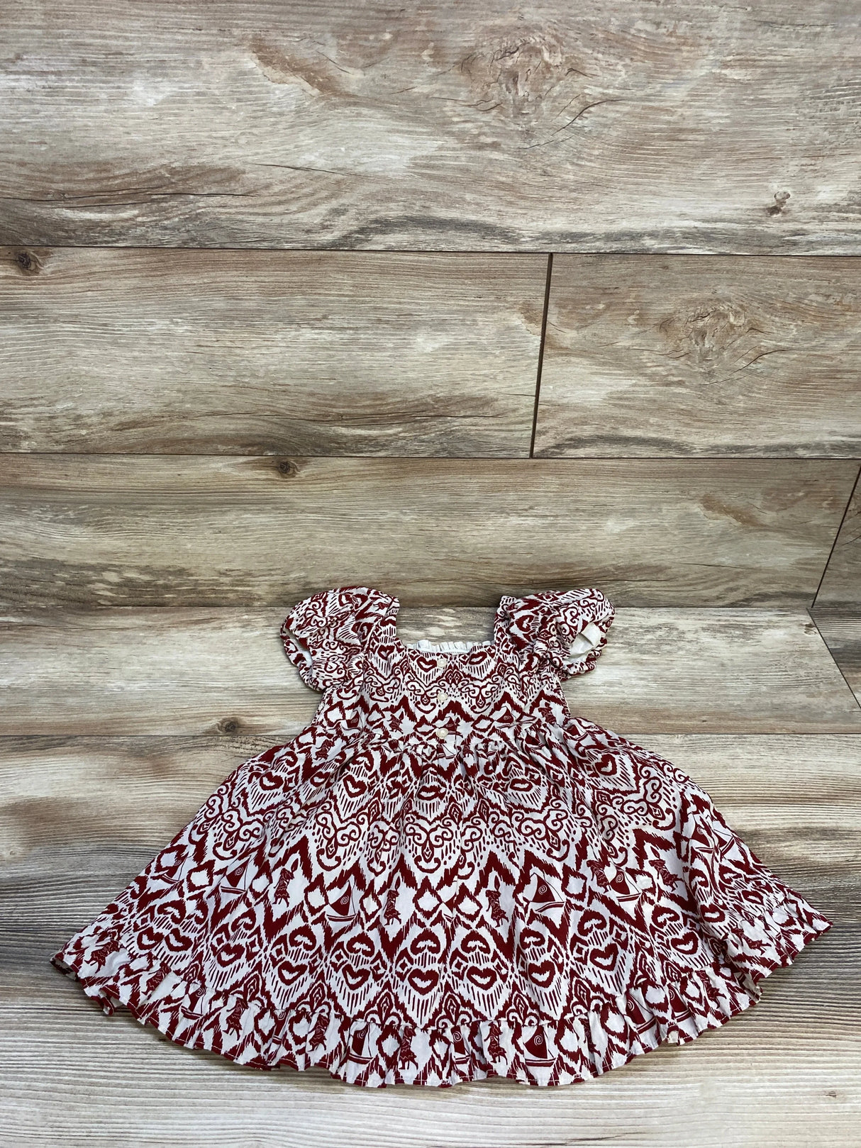 Red and white patterned baby dress with puff sleeves on wooden floor background