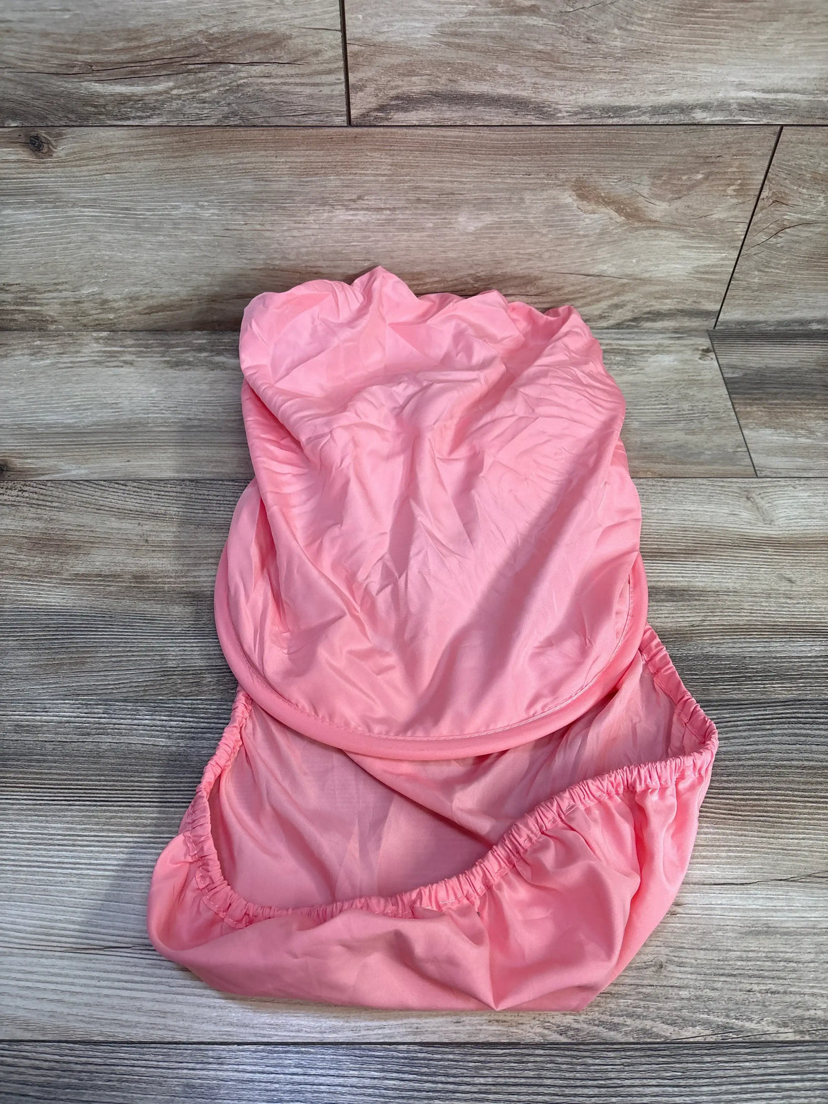 Top view of grapefruit pink sun and bug car seat cover showing pull-over flap and elasticized opening on wood-look floor