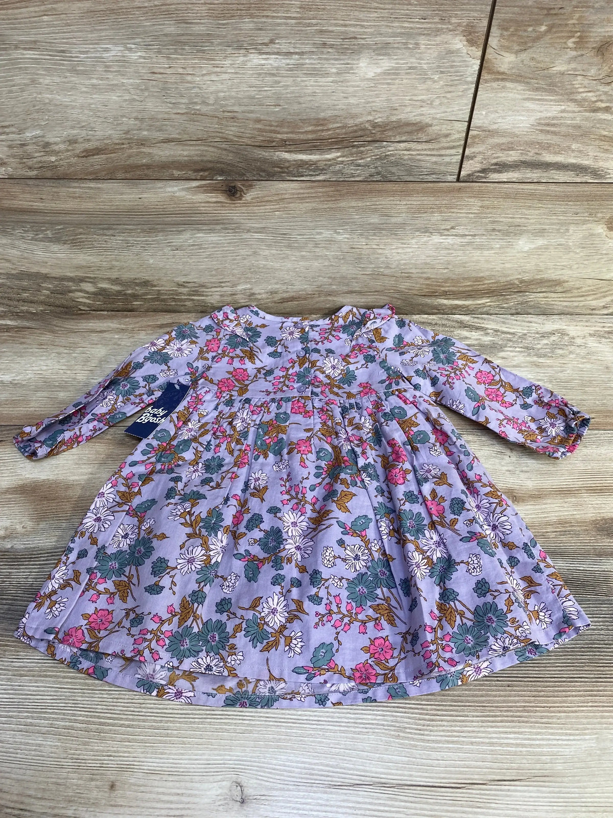 Flat lay of purple floral toddler dress showcasing ruffled skirt and long sleeves, size 18 months, on light wood background