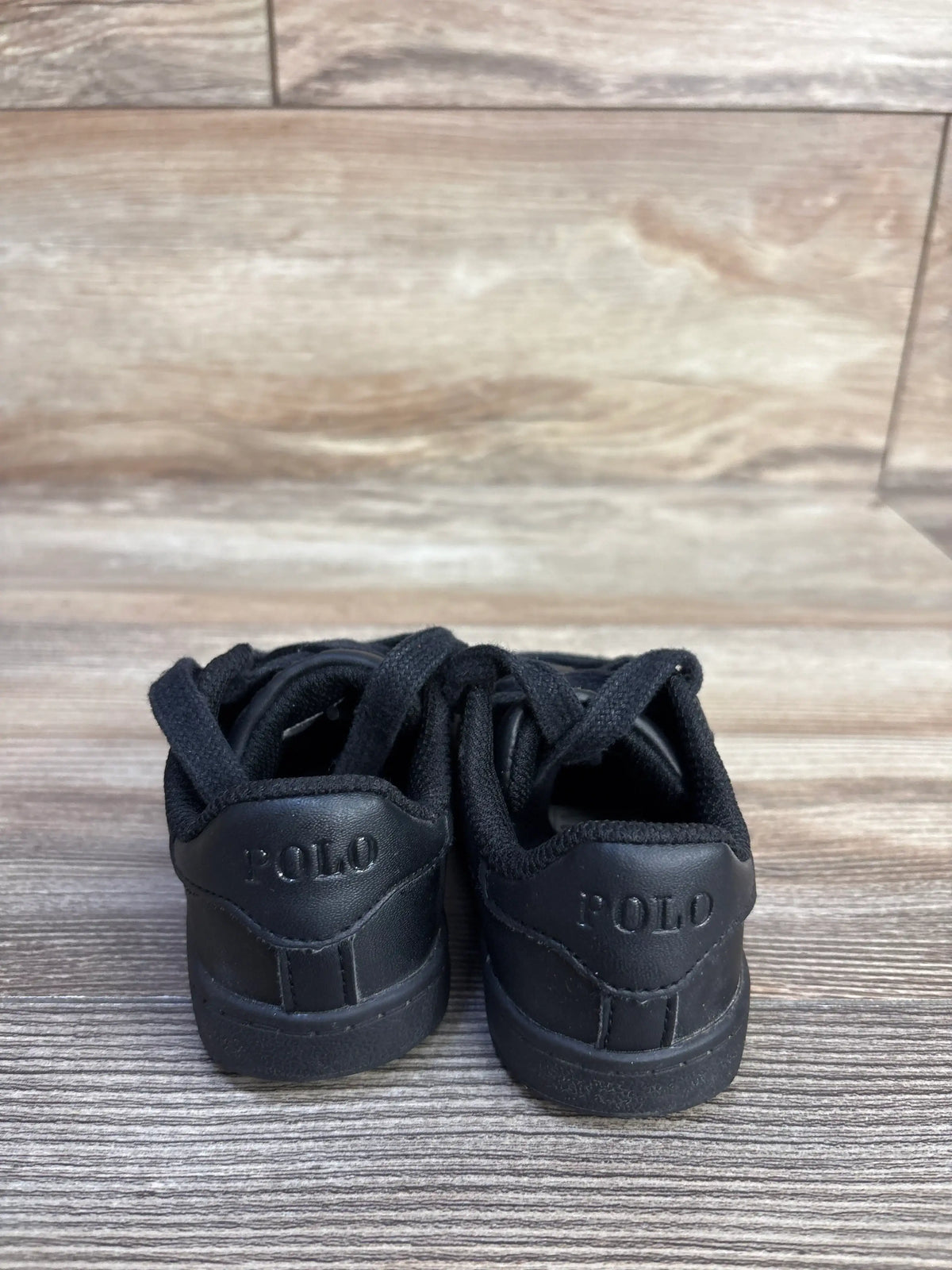 Rear view of Polo Ralph Lauren Quilton Bear black sneakers in size 6C showcasing embossed POLO heels on a wood-look floor