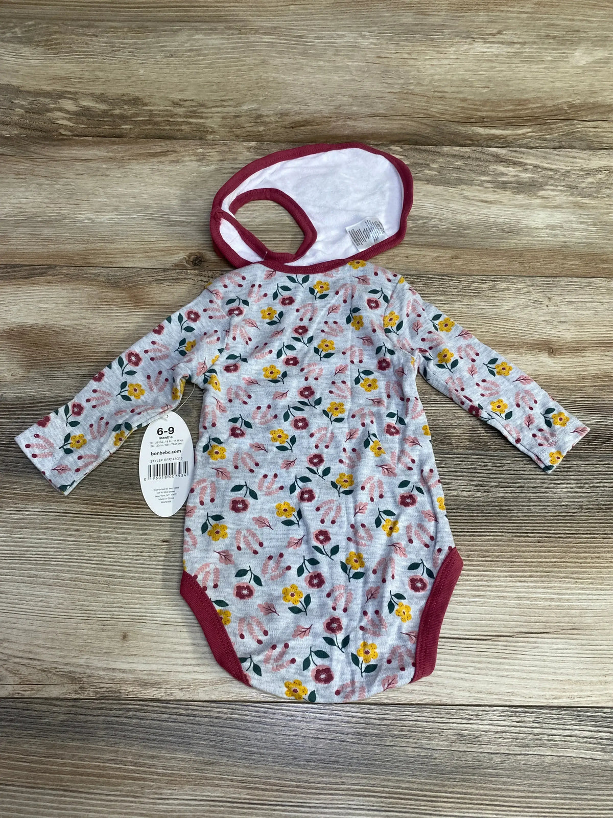 Flat lay of grey long-sleeve floral baby bodysuit with matching burgundy-trim bib on wood background