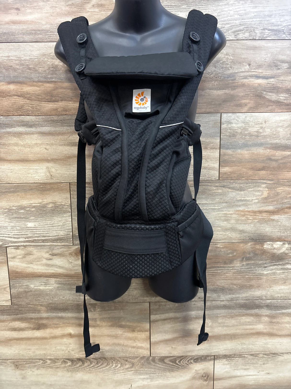 Front view of Ergobaby Omni Breeze black baby carrier on mannequin showing padded straps, head support and wide waist belt on wood background