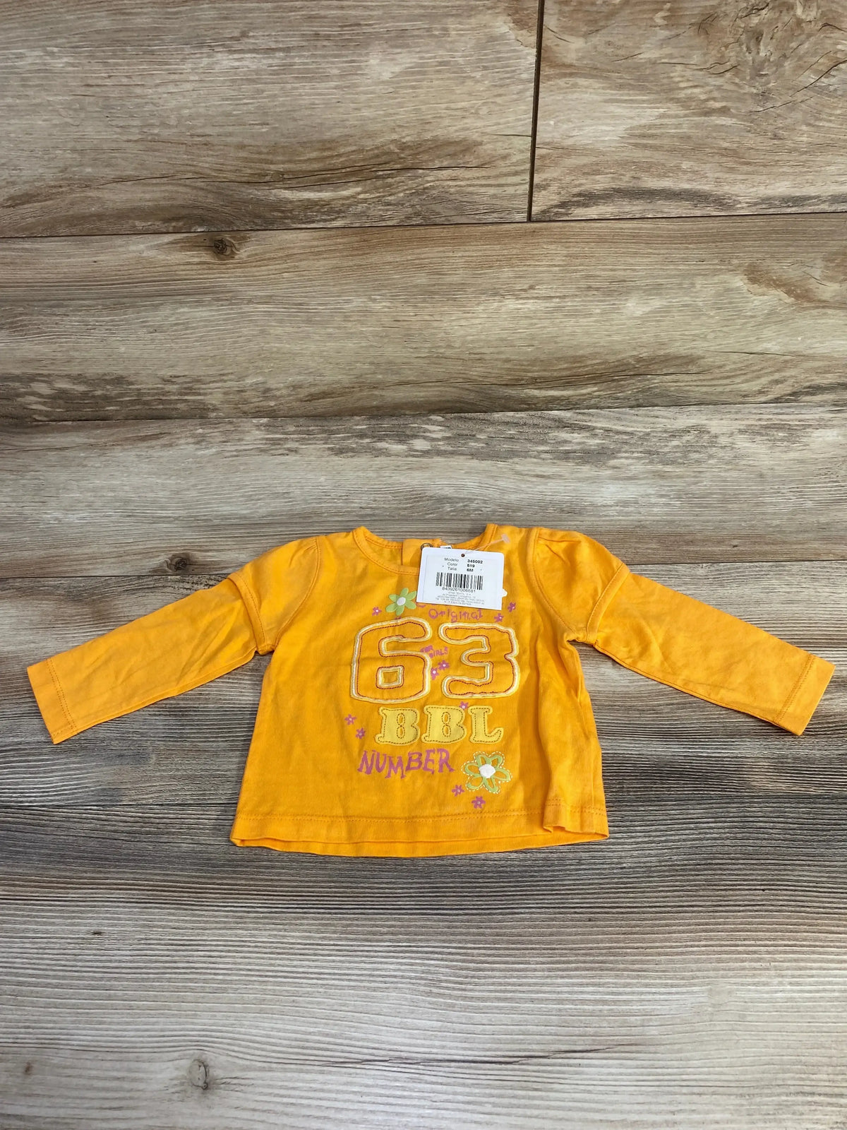 Flat lay of orange Boboli long-sleeve baby shirt (3–6M) showing embroidered 63 and flower print on wood floor