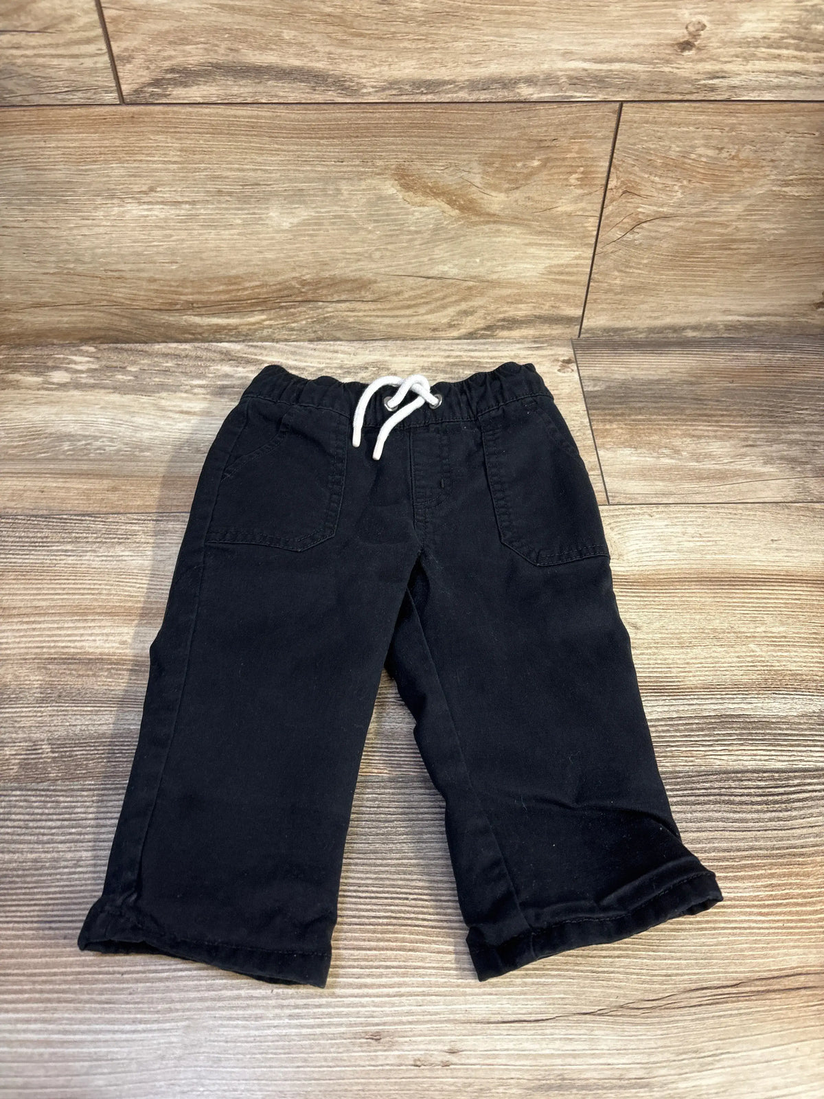 Top view of black Cat and Jack lined drawstring pants with elastic waist, white drawstring and patch pockets on wood floor