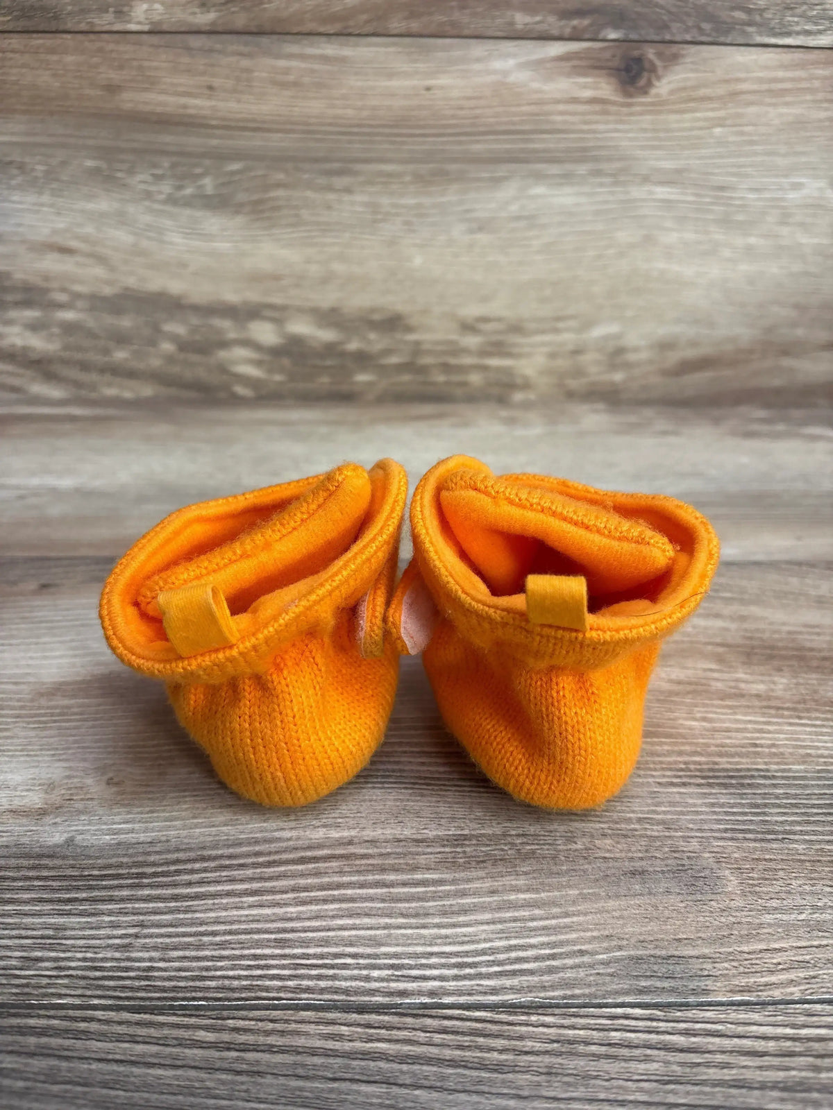 Front view of Cat & Jack pumpkin crib booties size 3C showcasing bright orange knit fabric and elastic cuffs on wood background