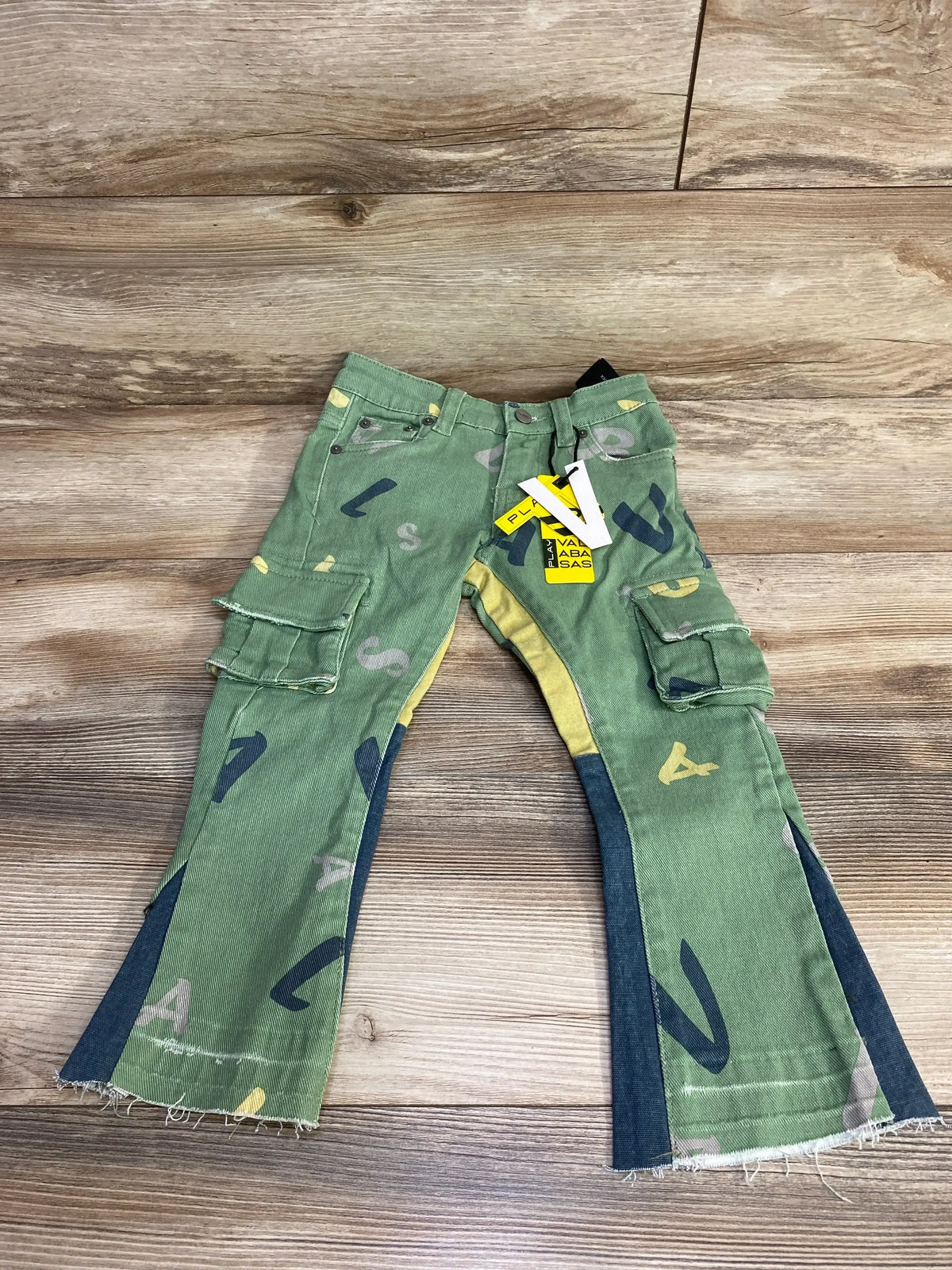 Flat lay of Valabasas cargo pants size 4T in green with cargo pockets, letter print and frayed hems on wood background