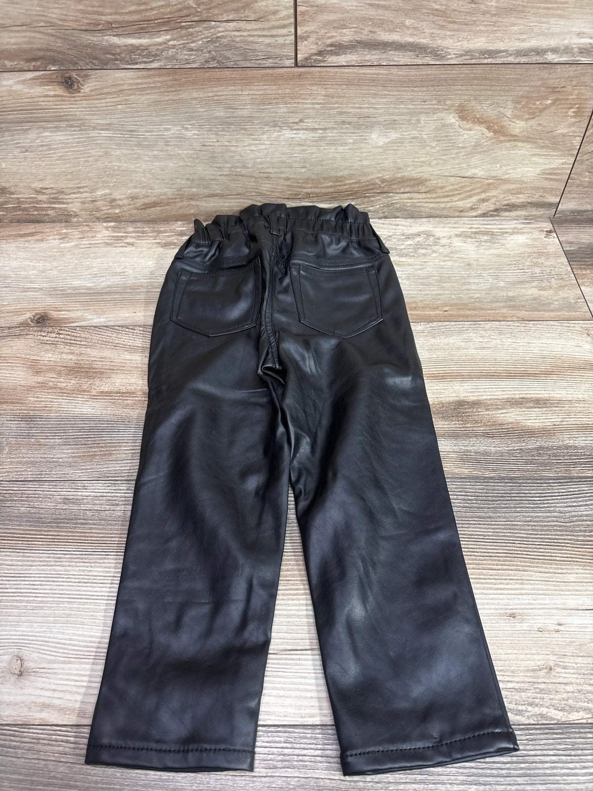 Back view of Baby Gap toddler black faux-leather pants with back pockets on wood floor