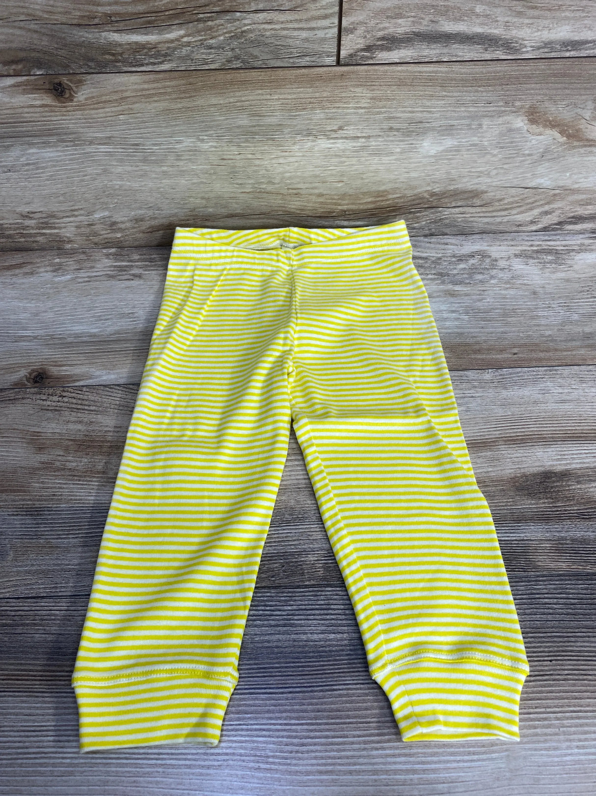 Flat lay of yellow and white striped toddler pull-on pants (18-24 months) showing elastic waistband and cuffed ankles on wood floor