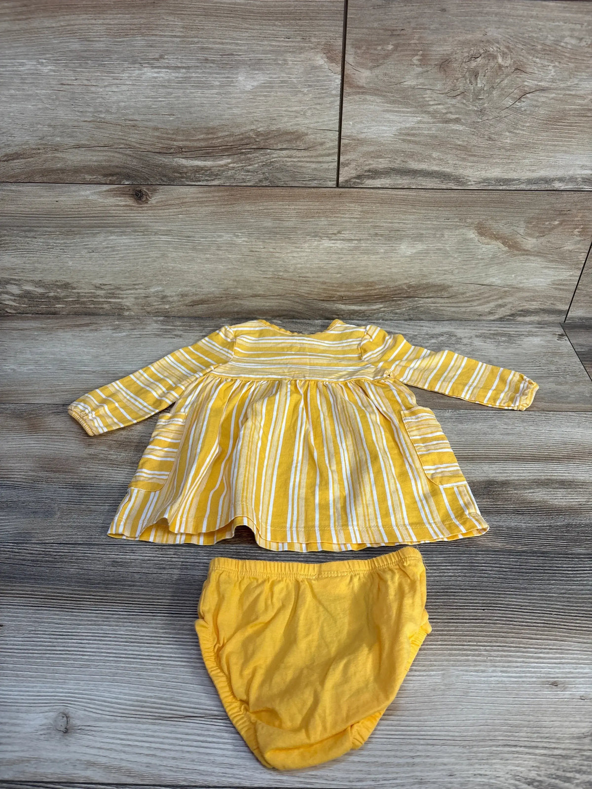 Flat lay front of yellow striped long-sleeve Henley dress with matching yellow bloomers showing side pockets on wood floor background